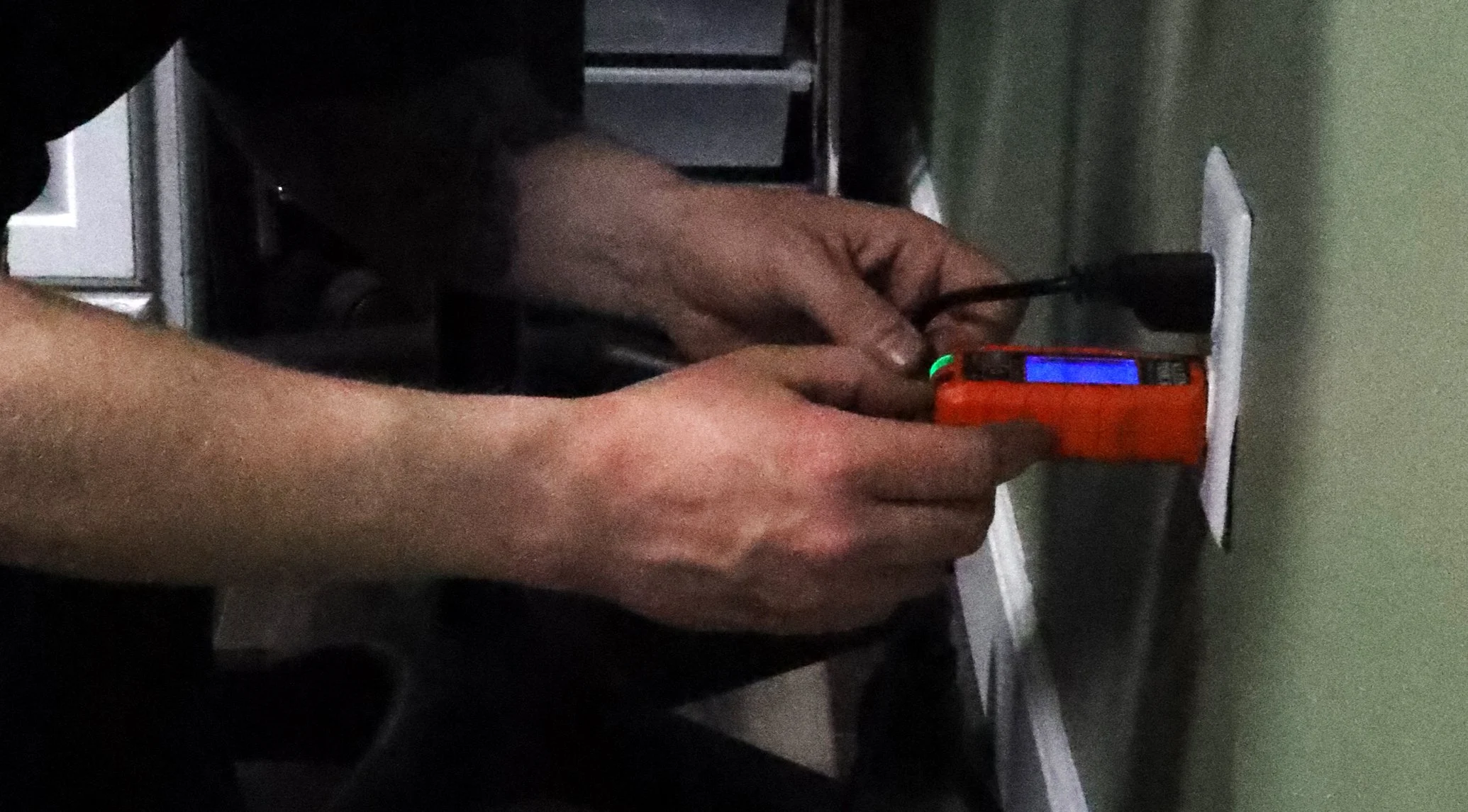 A person using a multimeter to test an electrical outlet on a wall.