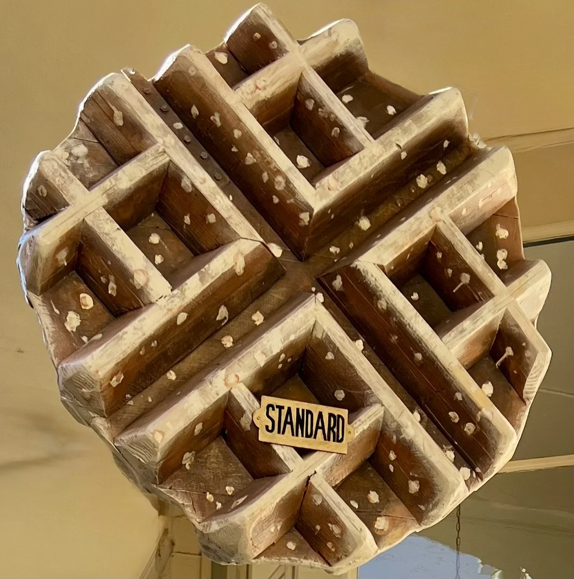 Upside-down large wooden wine rack with multiple square compartments, a small wooden sign labeled 'STANDARD' hanging in front.