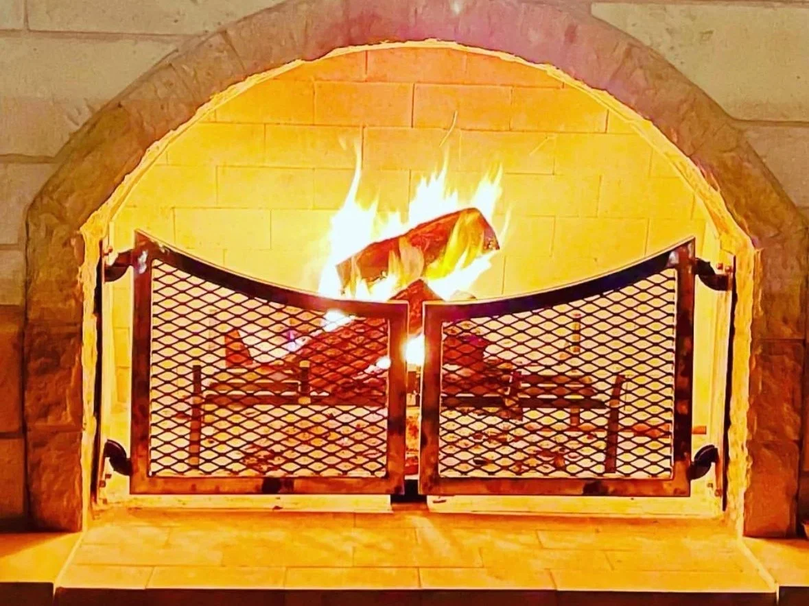 A fireplace with a burning log inside, protected by a metal mesh screen.