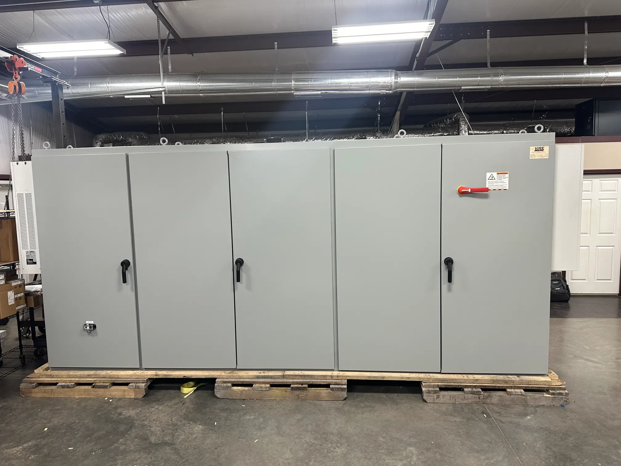 Large grey electrical or mechanical control cabinet on a wooden pallet in an industrial or warehouse setting.