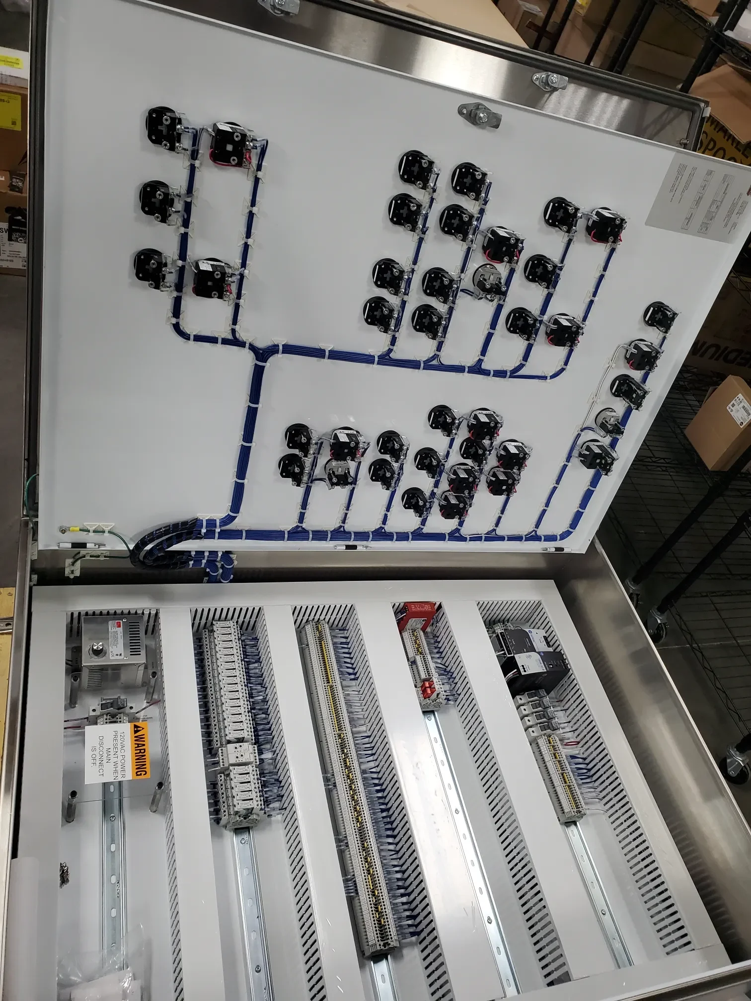Open electrical panel with various wiring and components, including terminal blocks, circuit breakers, and wiring conduits, mounted inside a metal enclosure.