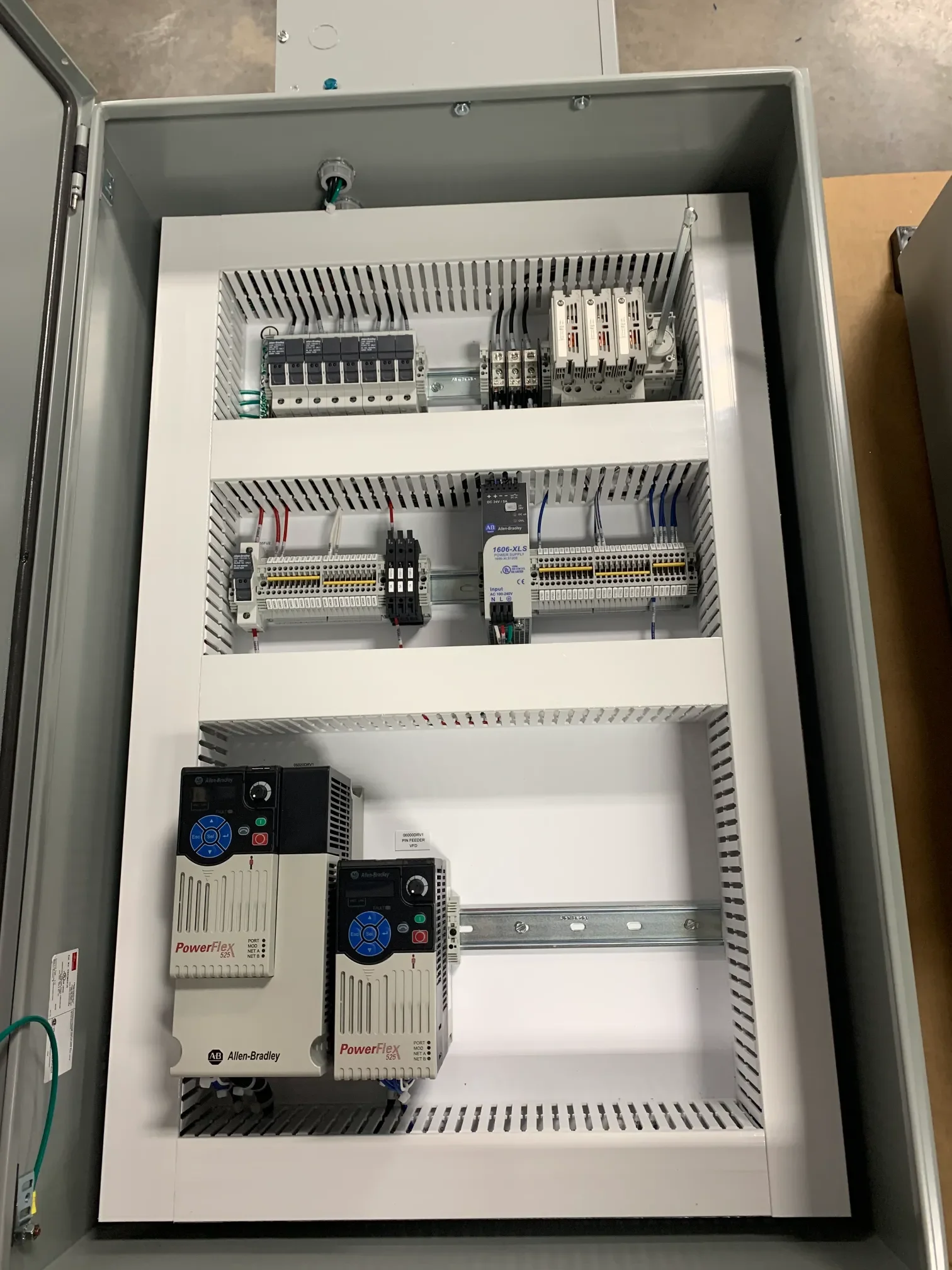 An electrical control panel with various circuit breakers, relays, and power supplies mounted inside an open gray metal enclosure.
