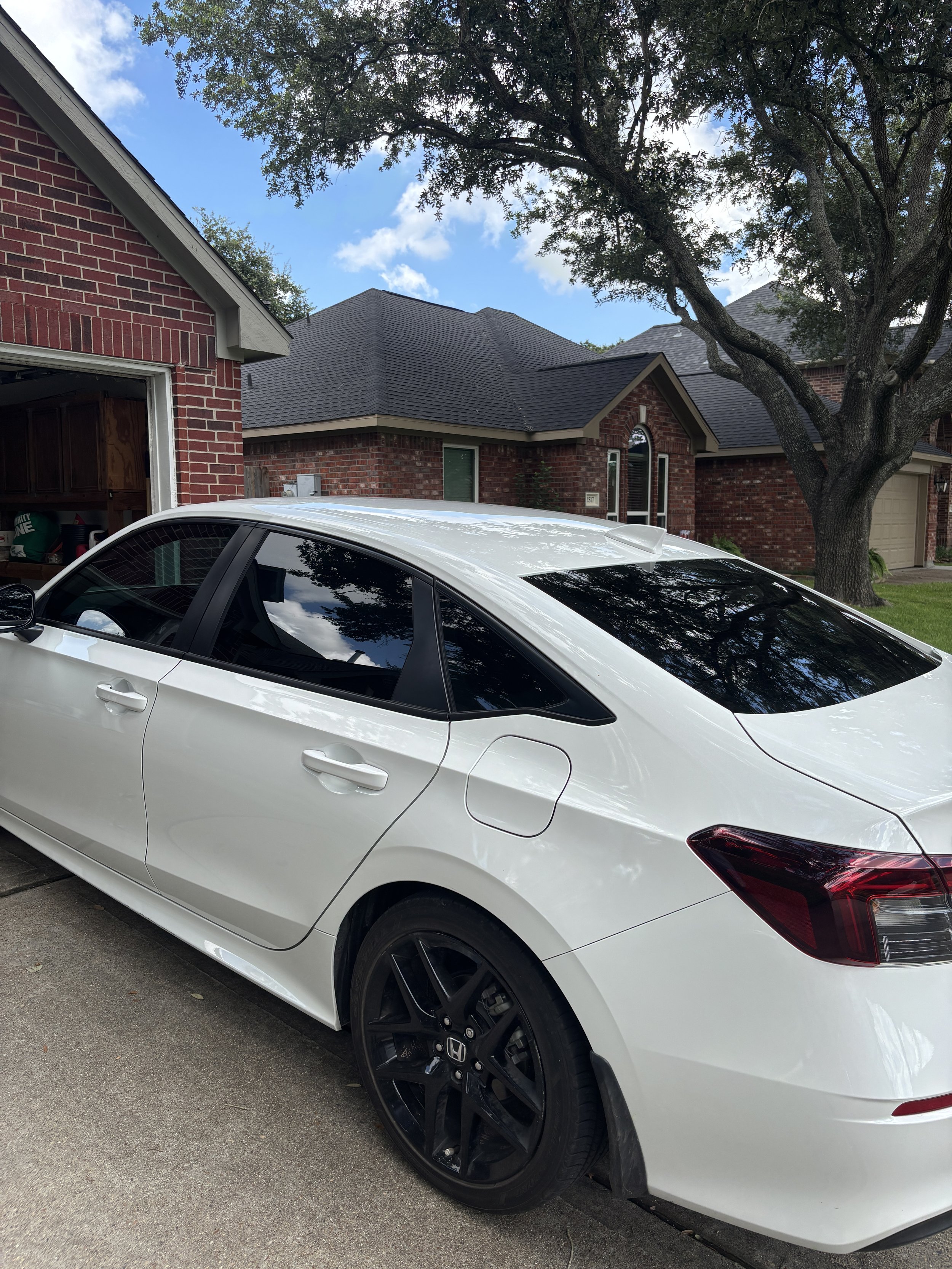 A white Honda Civic parked in a residential driveway with a brick house and a tree in the background.