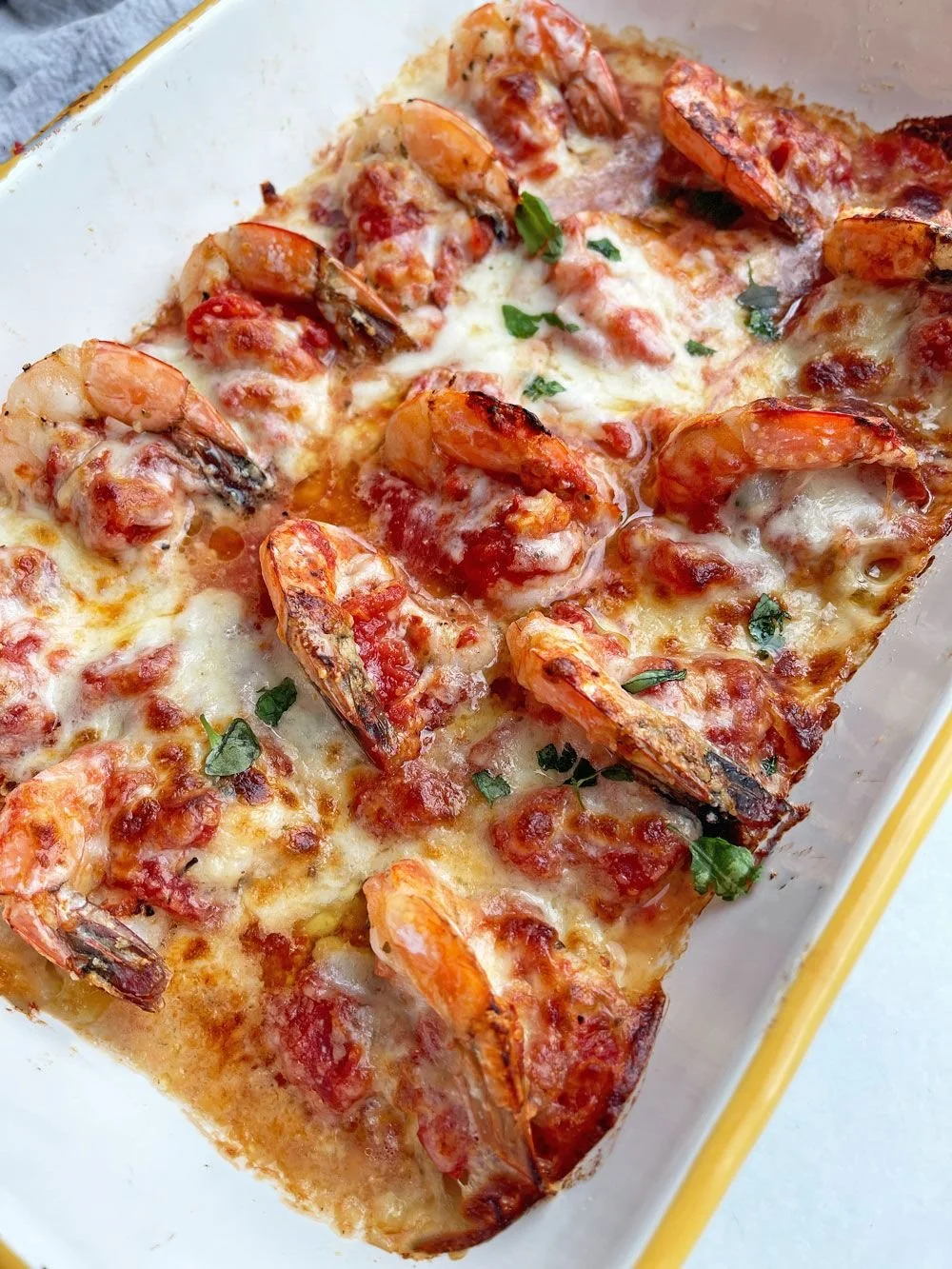 Baked shrimp and cheese casserole with melted cheese and garnished with chopped herbs.