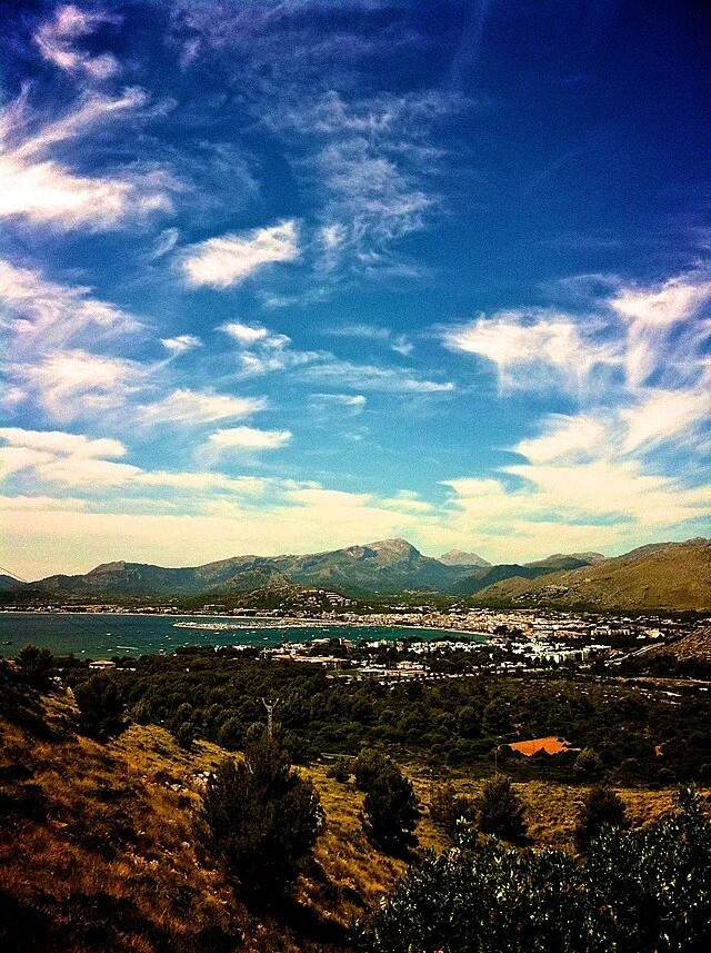 Scenic view of mountains, a lake, and a small town under a partly cloudy sky.