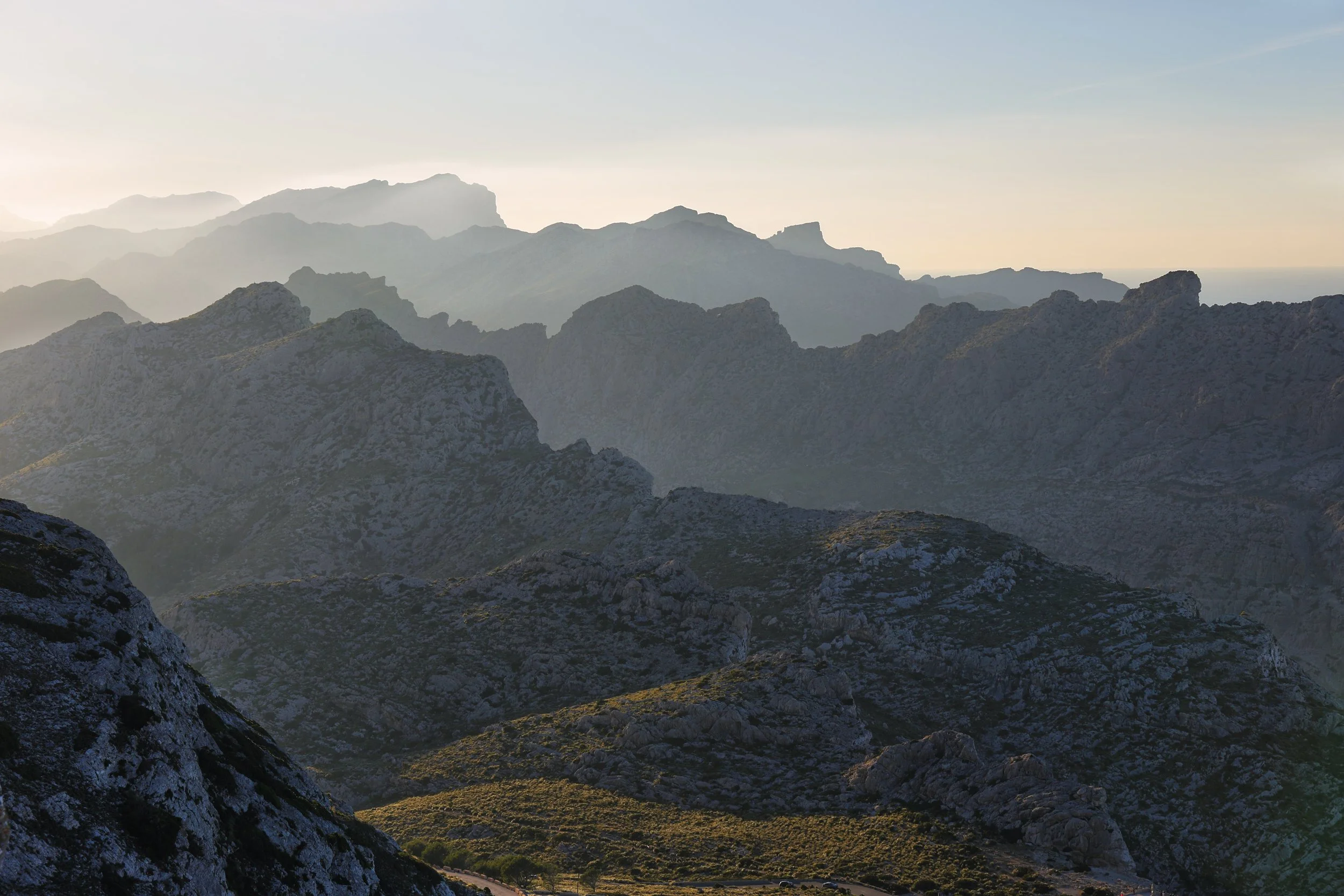 Mountain range with multiple ridges, some covered in greenery, under a clear sky.