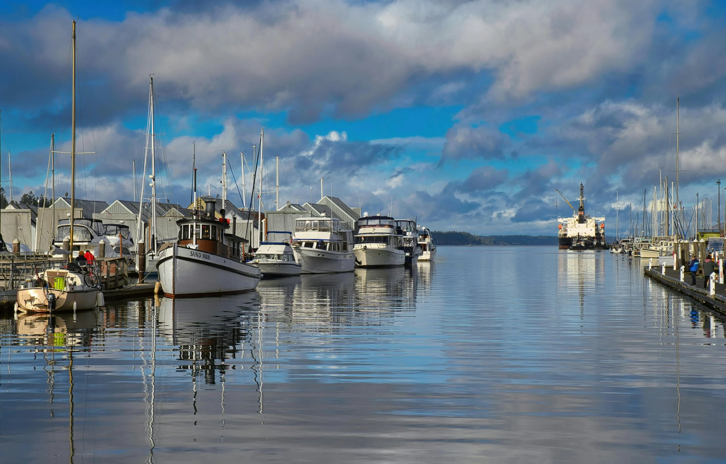 Marina with boats docked, cloudy sky, and calm water reflecting the boats and sky.