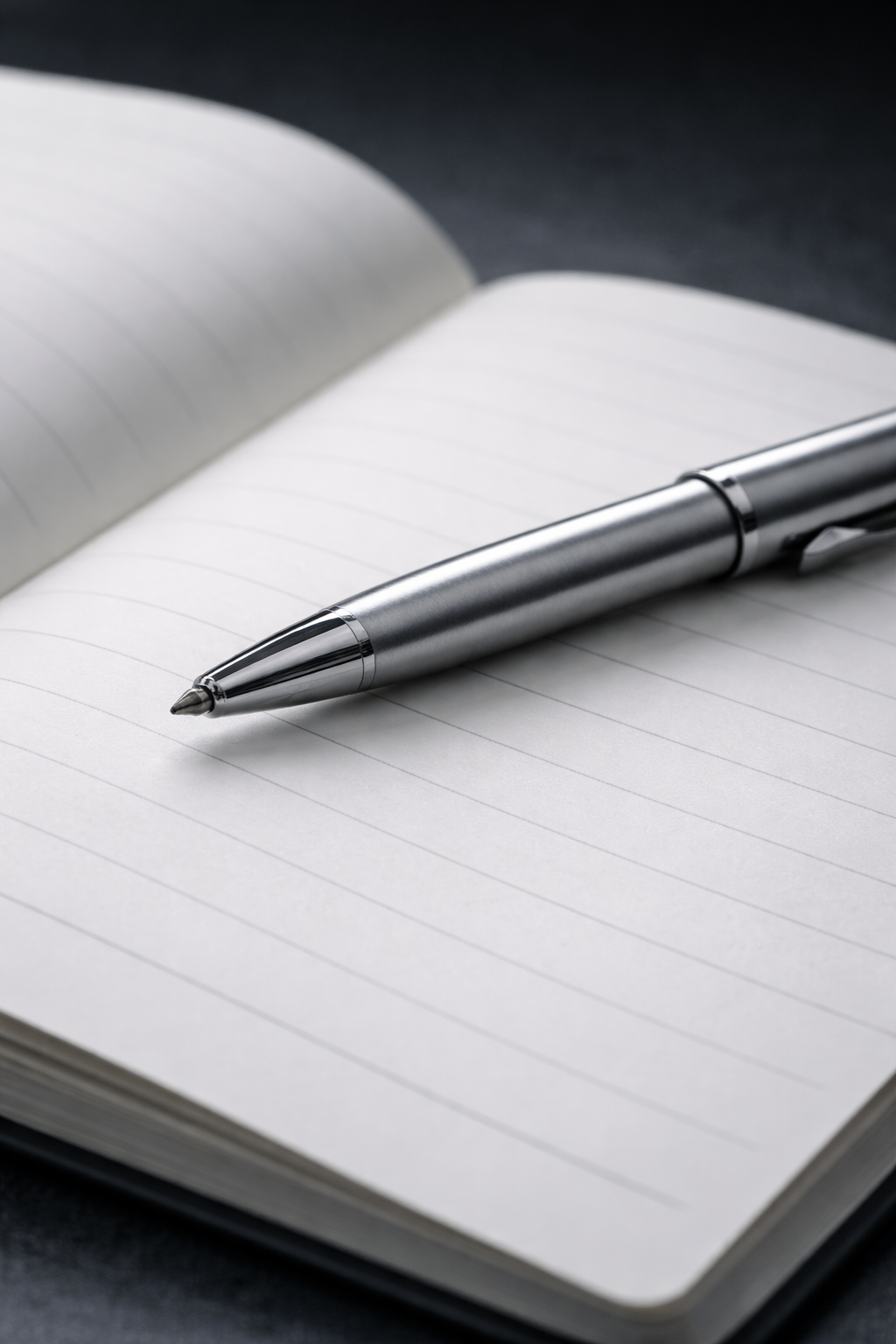 A silver pen resting on an open lined notebook with blank pages.