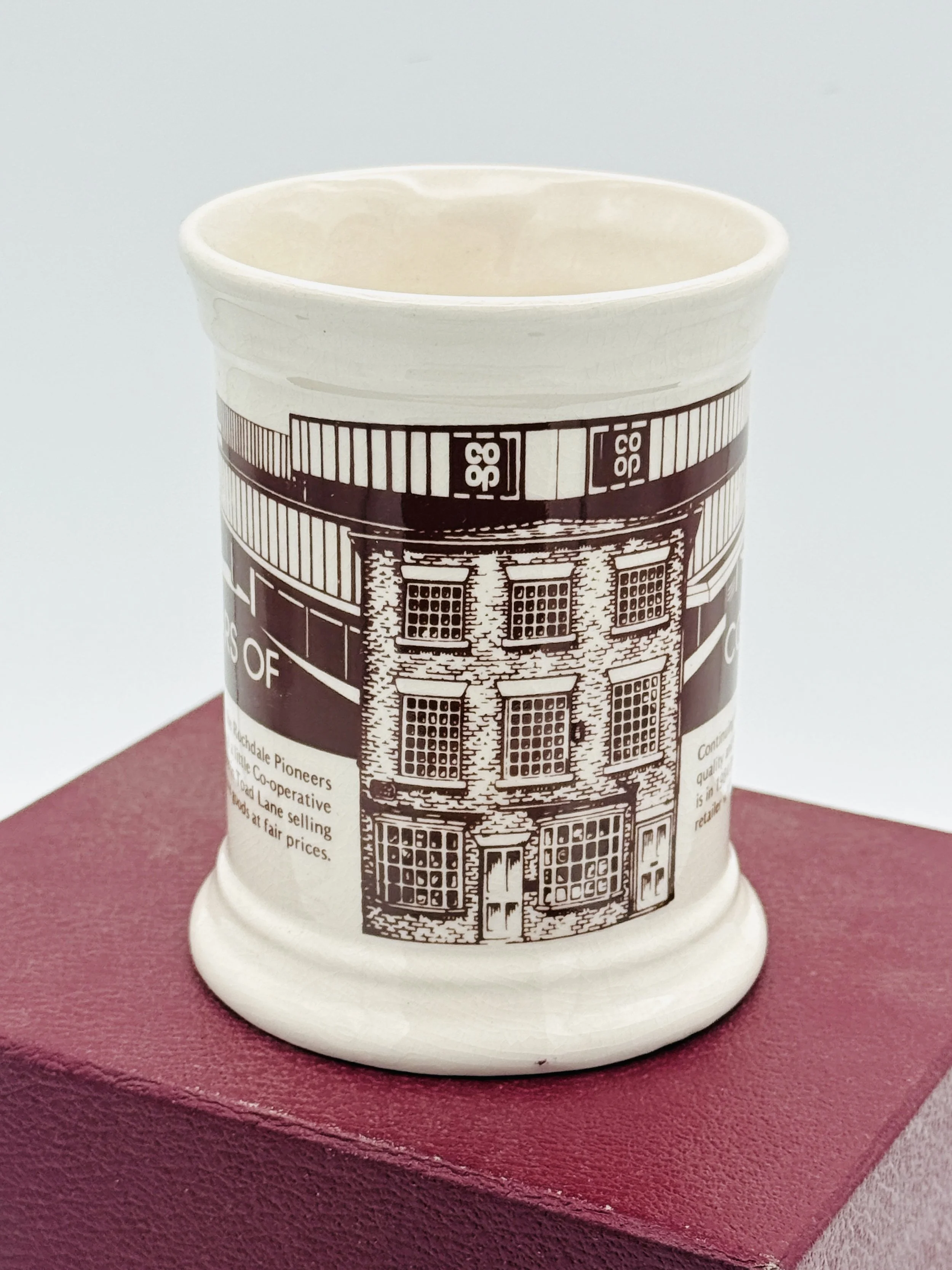 Ceramic mug with a black and white illustration of a historic brick building, placed on a red surface.