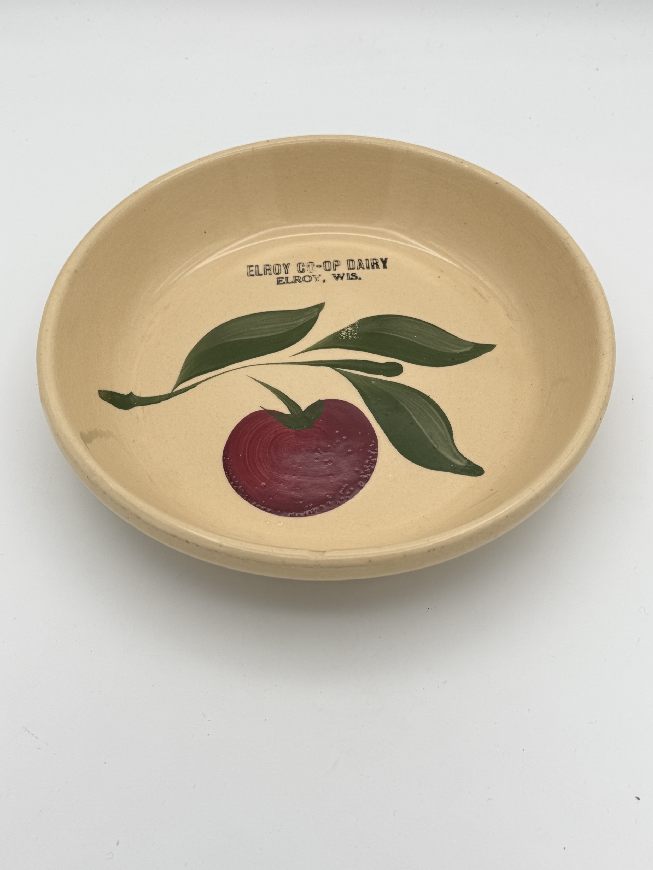 Round ceramic dish with a painted red fruit, green leaves, and text that reads 'Elroy Co-op Dairy Elroy, Wis.'