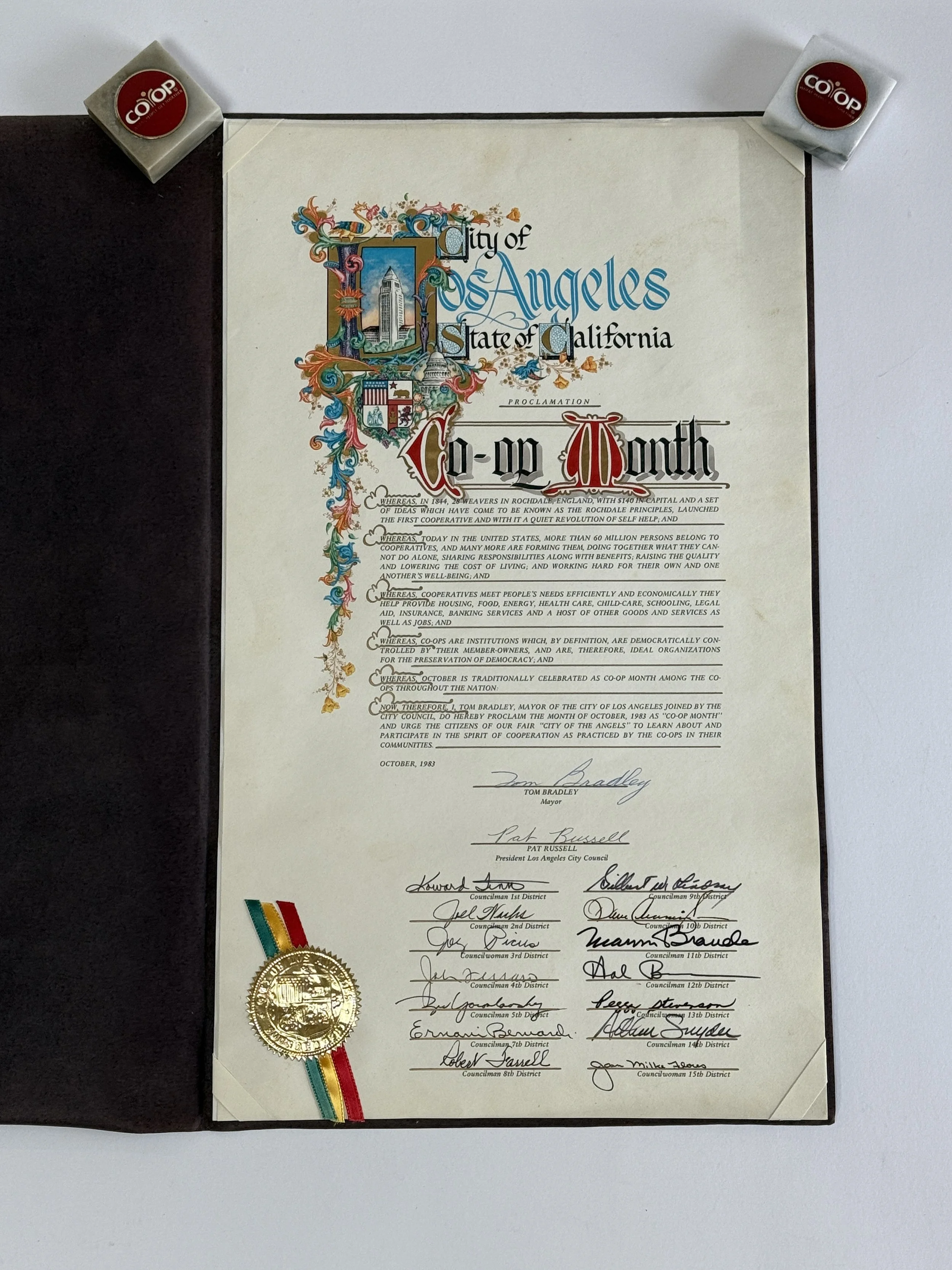 Official city proclamation document from Los Angeles, California, celebrating Co-op Month, dated October 1983, with signatures and a gold seal, accompanied by two small Co-op insignia badges.