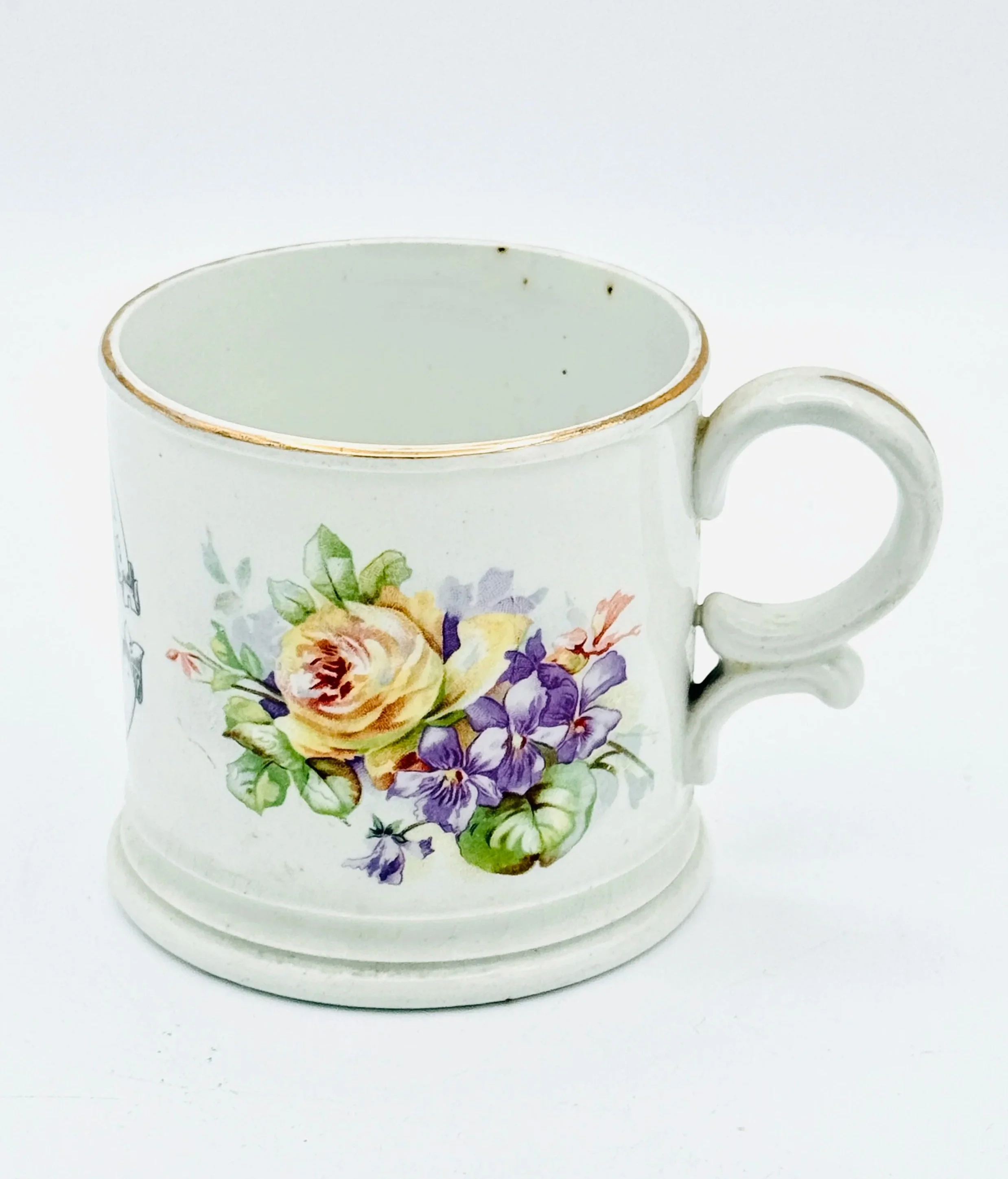 White ceramic mug with floral pattern of yellow, purple, and green flowers, resting on a matching saucer with a gold rim.
