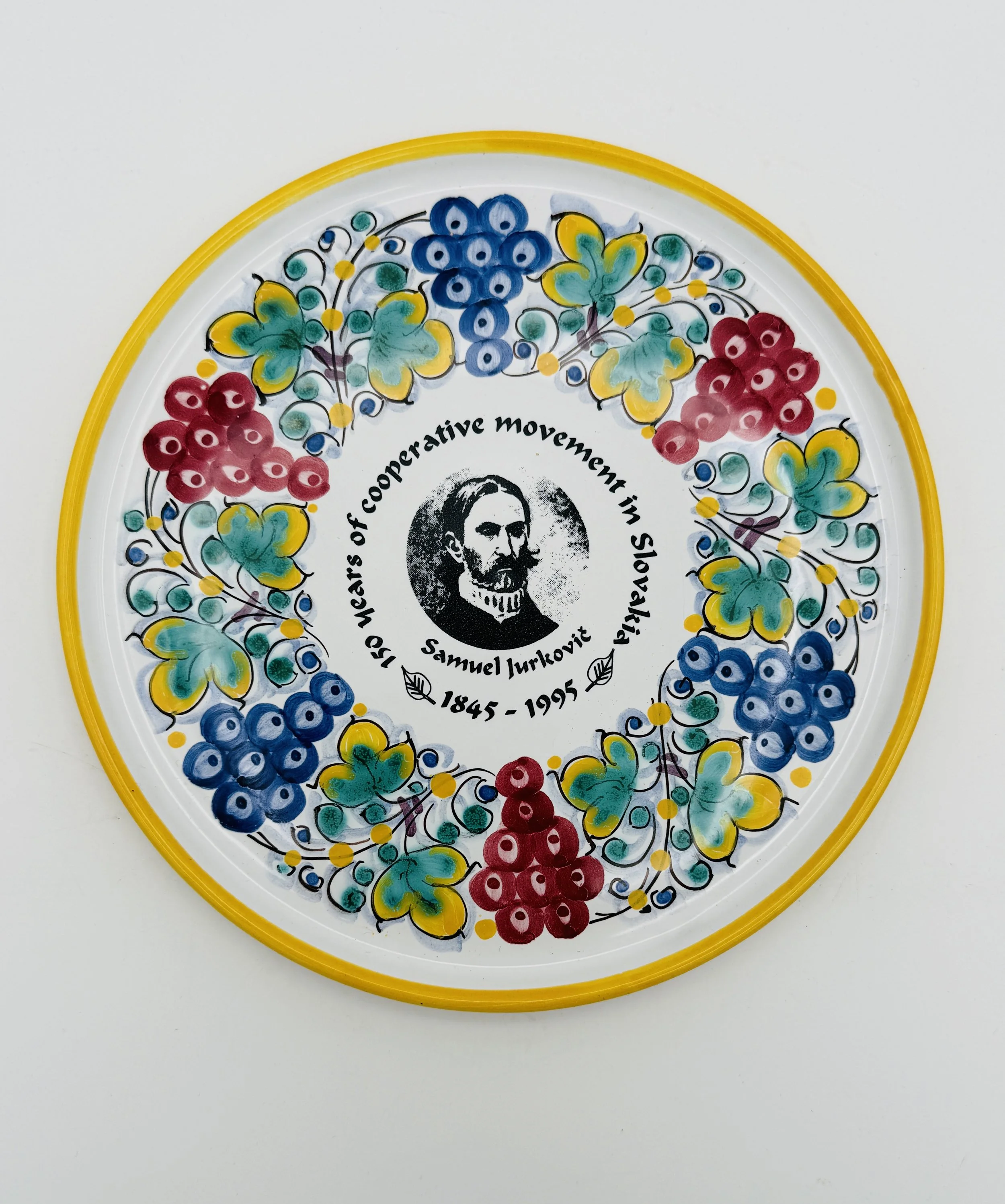 Decorative plate with a black and white portrait in the center of Samuel Turković, surrounded by colorful floral patterns in red, blue, yellow, and green, with text honoring 150 years of cooperative movement in Slavonia from 1845 to 1995.