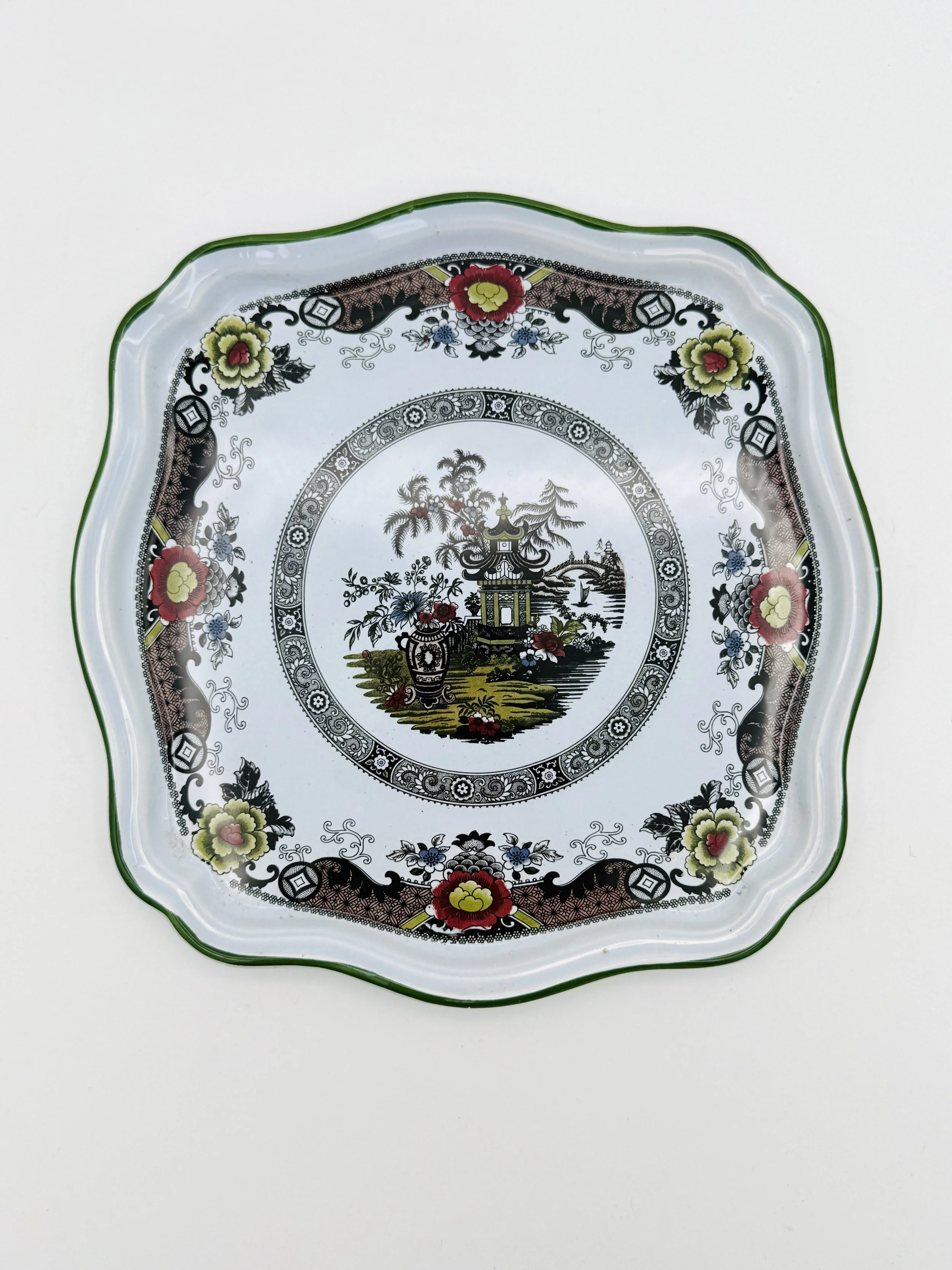 Decorative ceramic plate with intricate Asian-inspired patterns, featuring a central scene of a pagoda, trees, and flowers, bordered by floral motifs and a green rim.