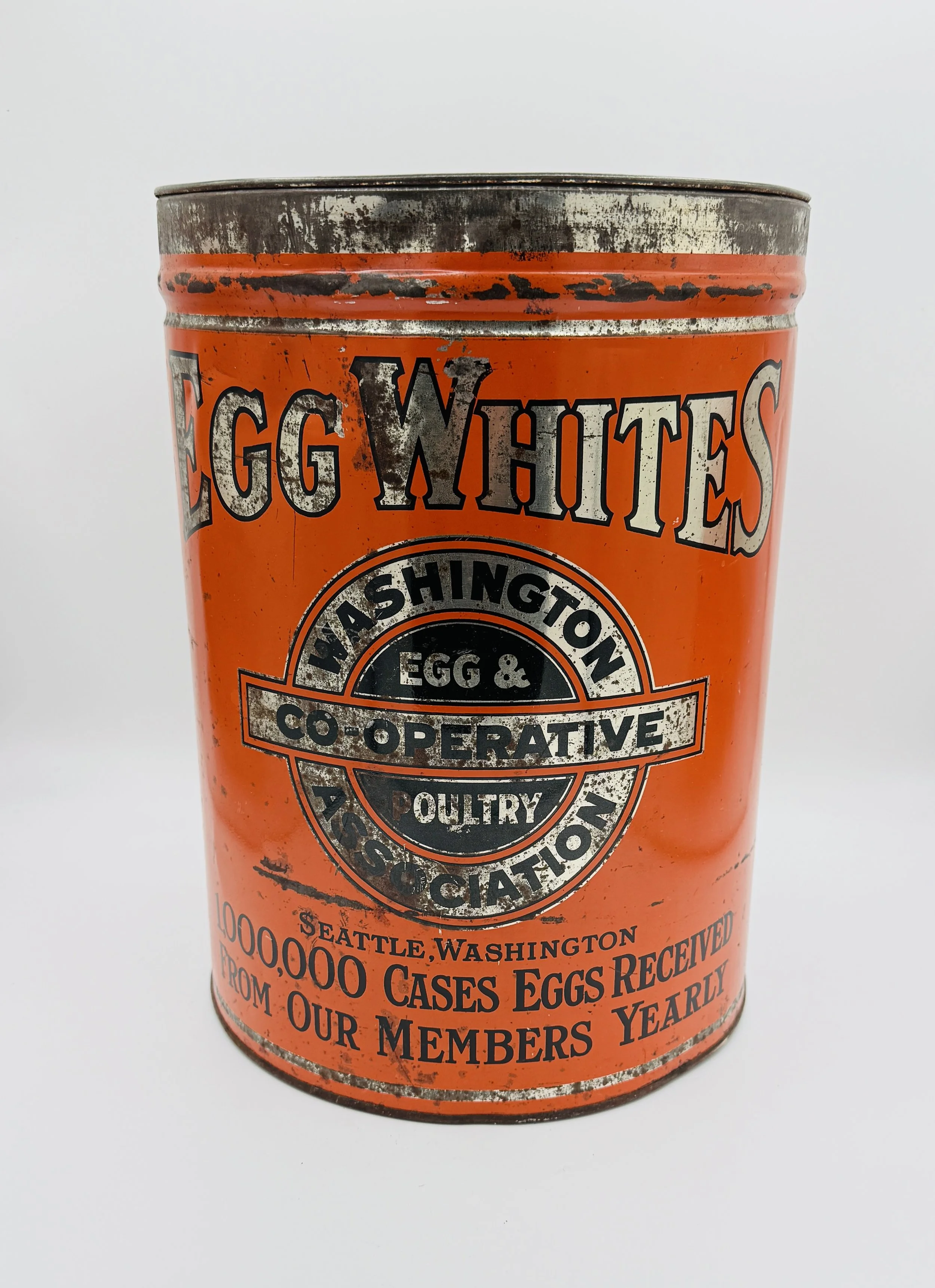 Orange vintage tin can with black and white text and emblem, labeled 'Egg Whites' from the Washington Egg & Co-operative Poultry Association, indicating 1,000,000 cases of eggs received annually in Seattle, Washington.