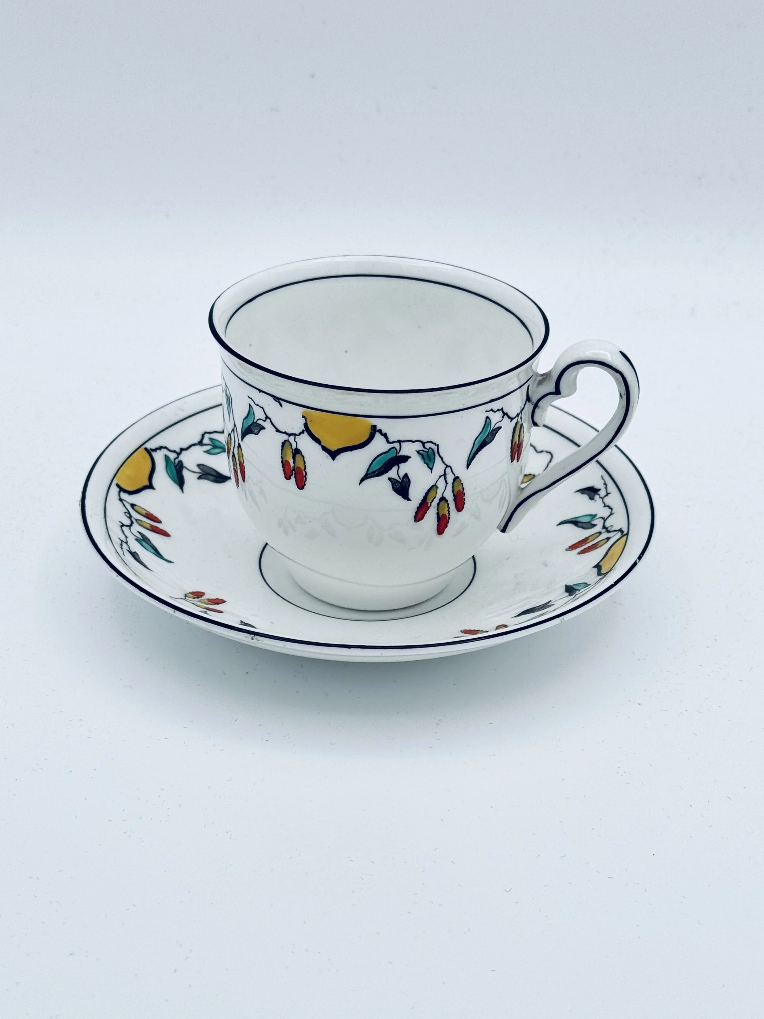 A white teacup and saucer with colorful floral and fruit pattern on a white background.