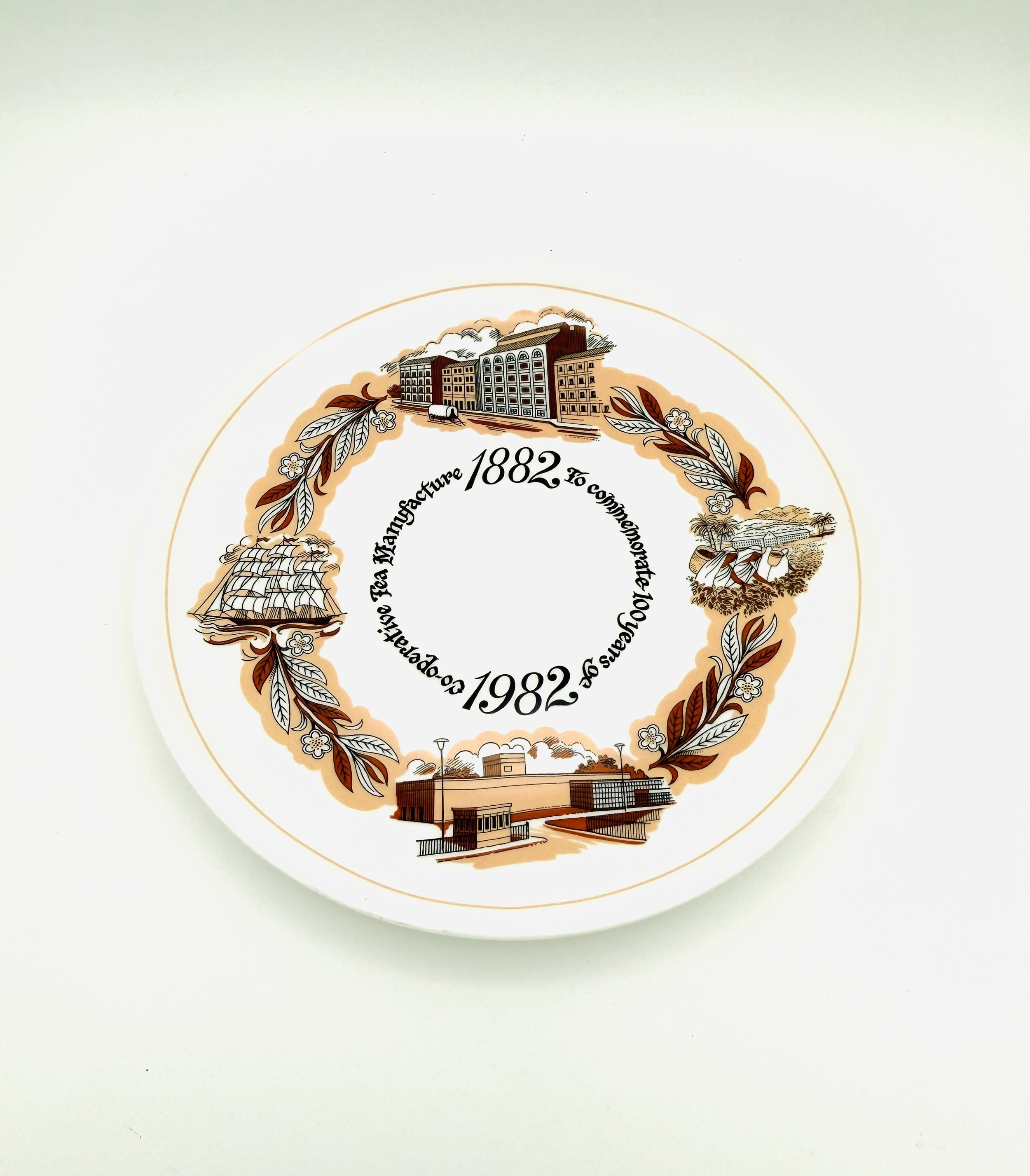 Circular emblem with historical buildings, ships, factory, and laurel leaves, with dates 1882 and 1982, and the phrase 'To commemorate 100 years of operation, Fea Manufacturing'.