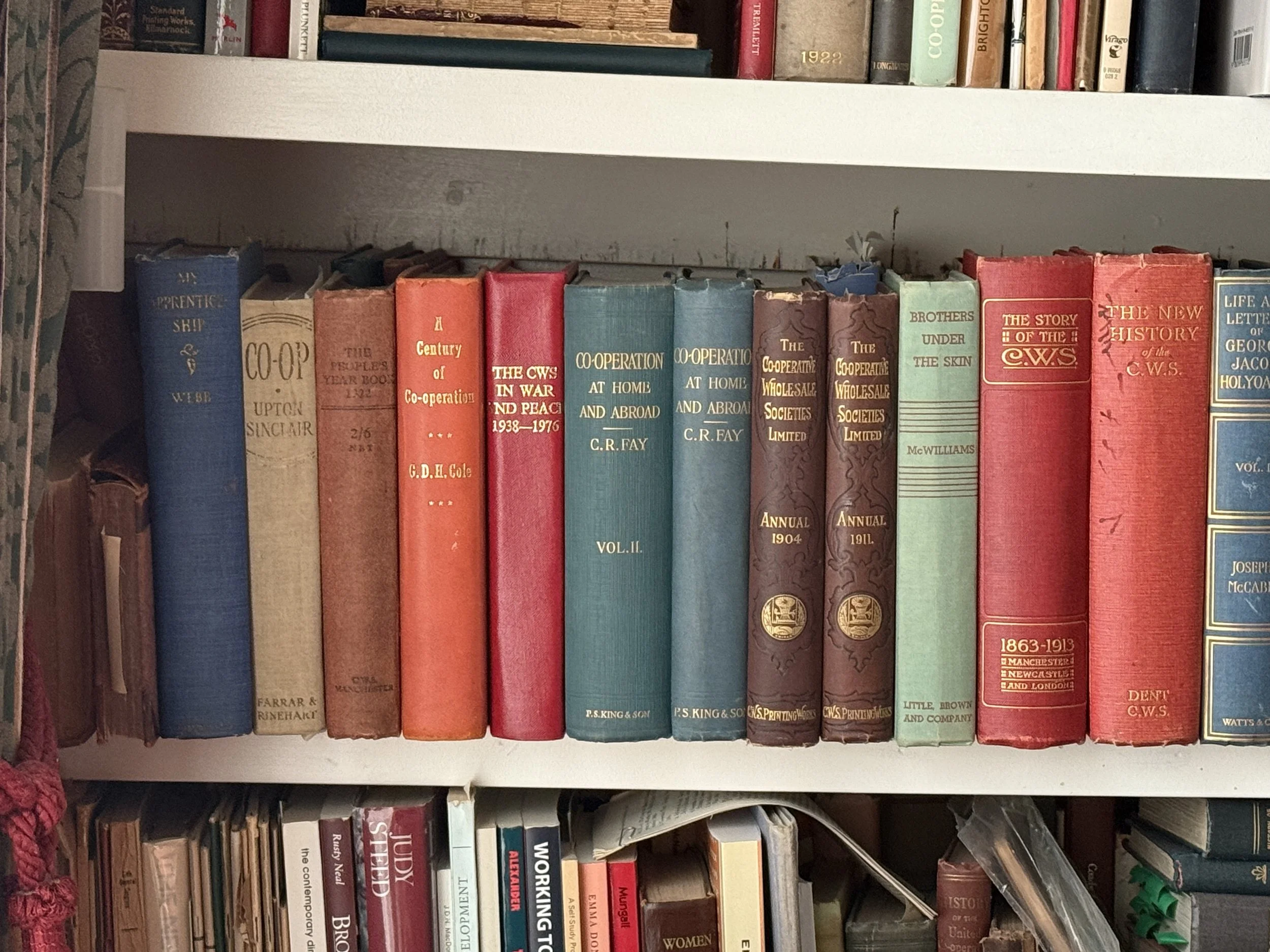 Books on a white bookshelf, with titles about history and cooperation, including 'The CWS in War and Peace 1938-1976' and 'The Story of the CWS'.