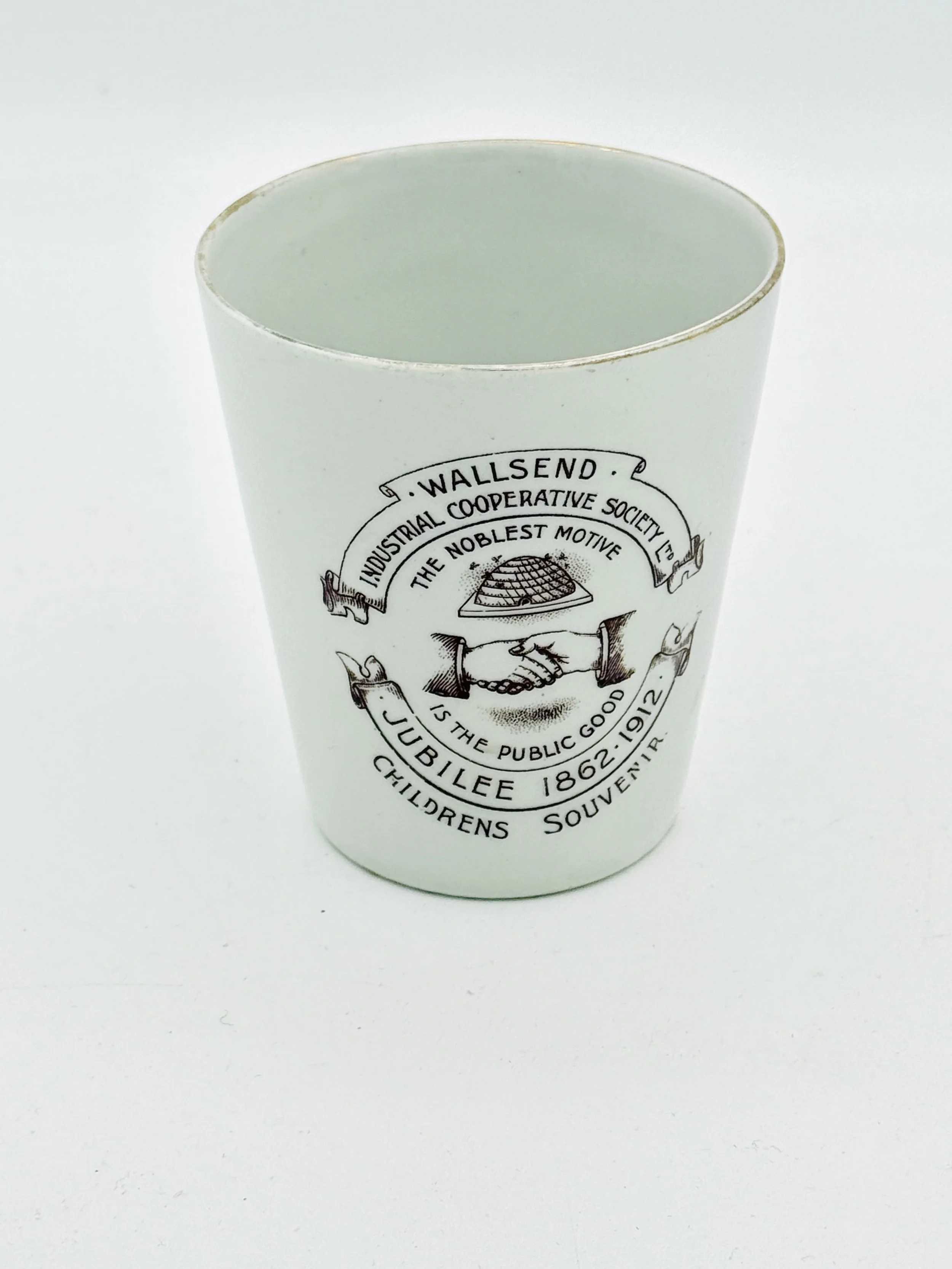 White ceramic mug with black text and design, featuring a handshake, a pie, and circular text referencing Wallsend Industrial Cooperative Society and Junilee, 1862-1912.