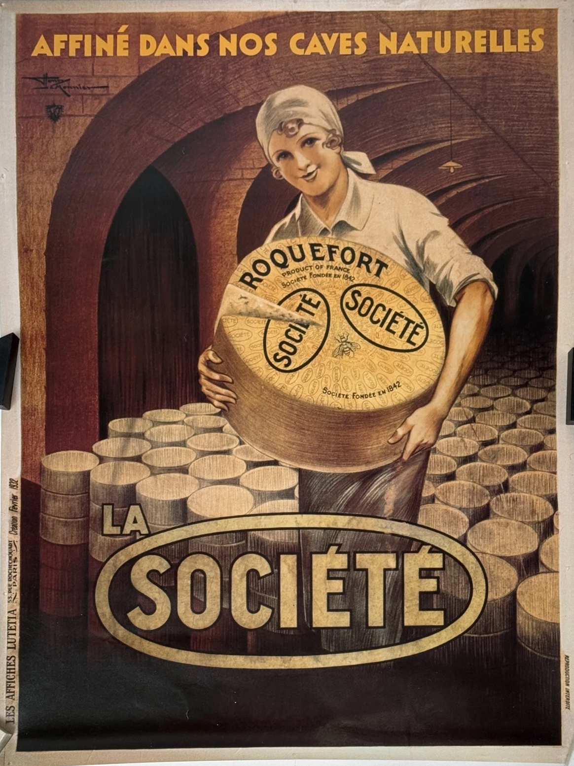 coop co-op Vintage poster depicting a woman with a smiling face holding a large wheel labeled "Société". The background shows stacks of barrels in a cellar. The text on the poster reads "Affiné dans nos caves naturelles" and "La Société".