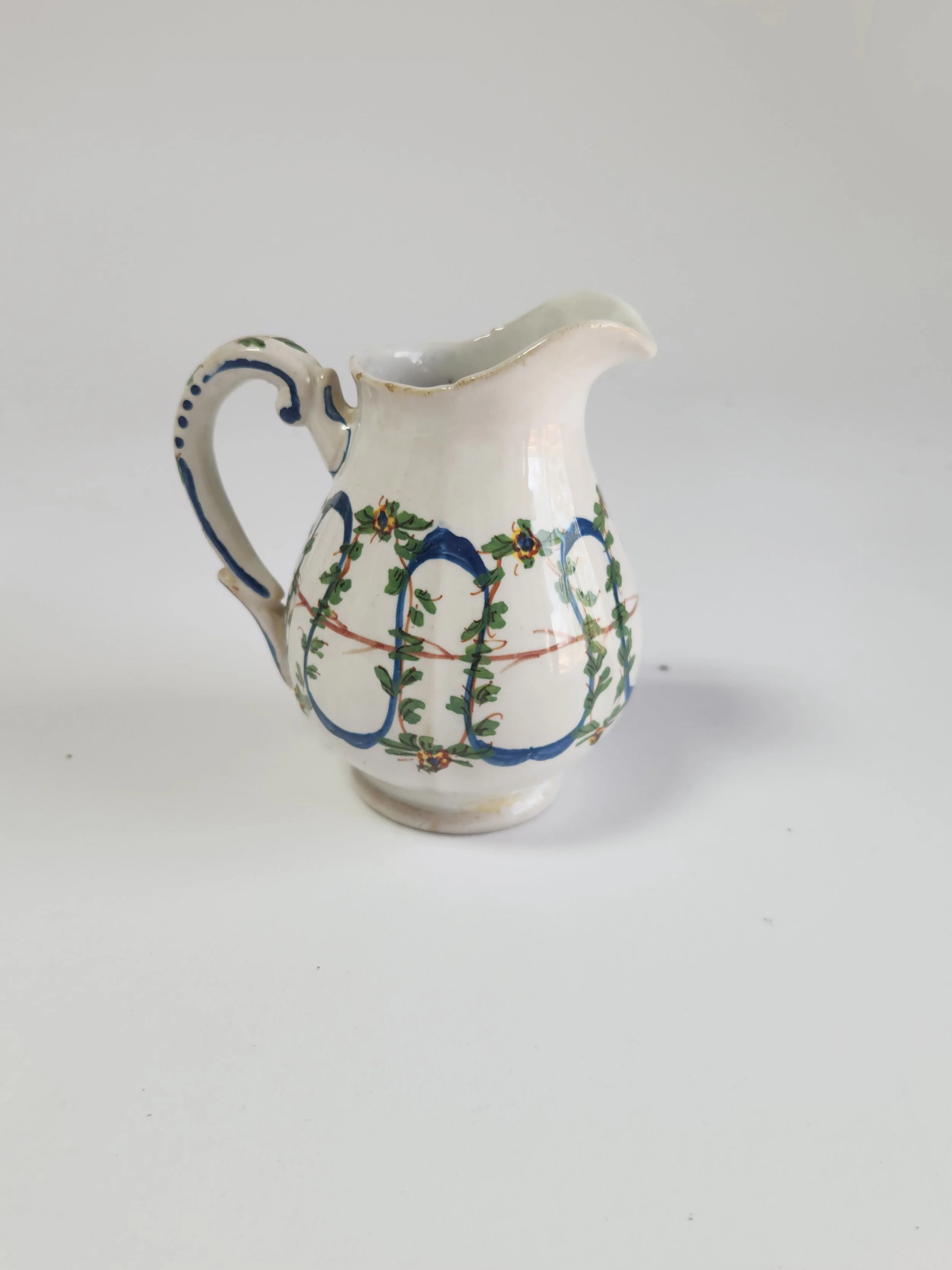 A small ceramic pitcher with decorative floral and blue patterns on a plain white background.