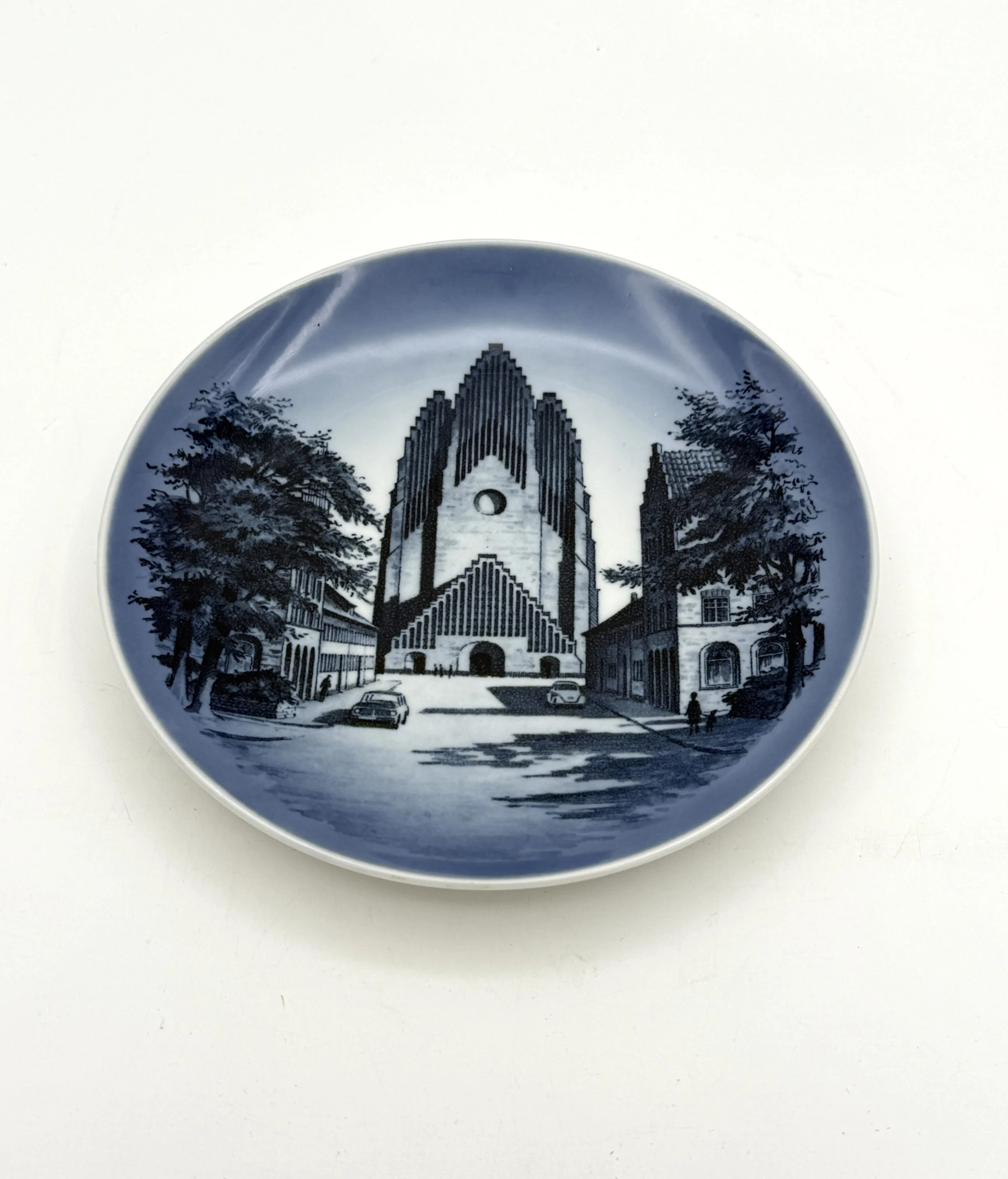 Decorative plate featuring a black and white cityscape with a modern cathedral and surrounding buildings, trees, and cars.