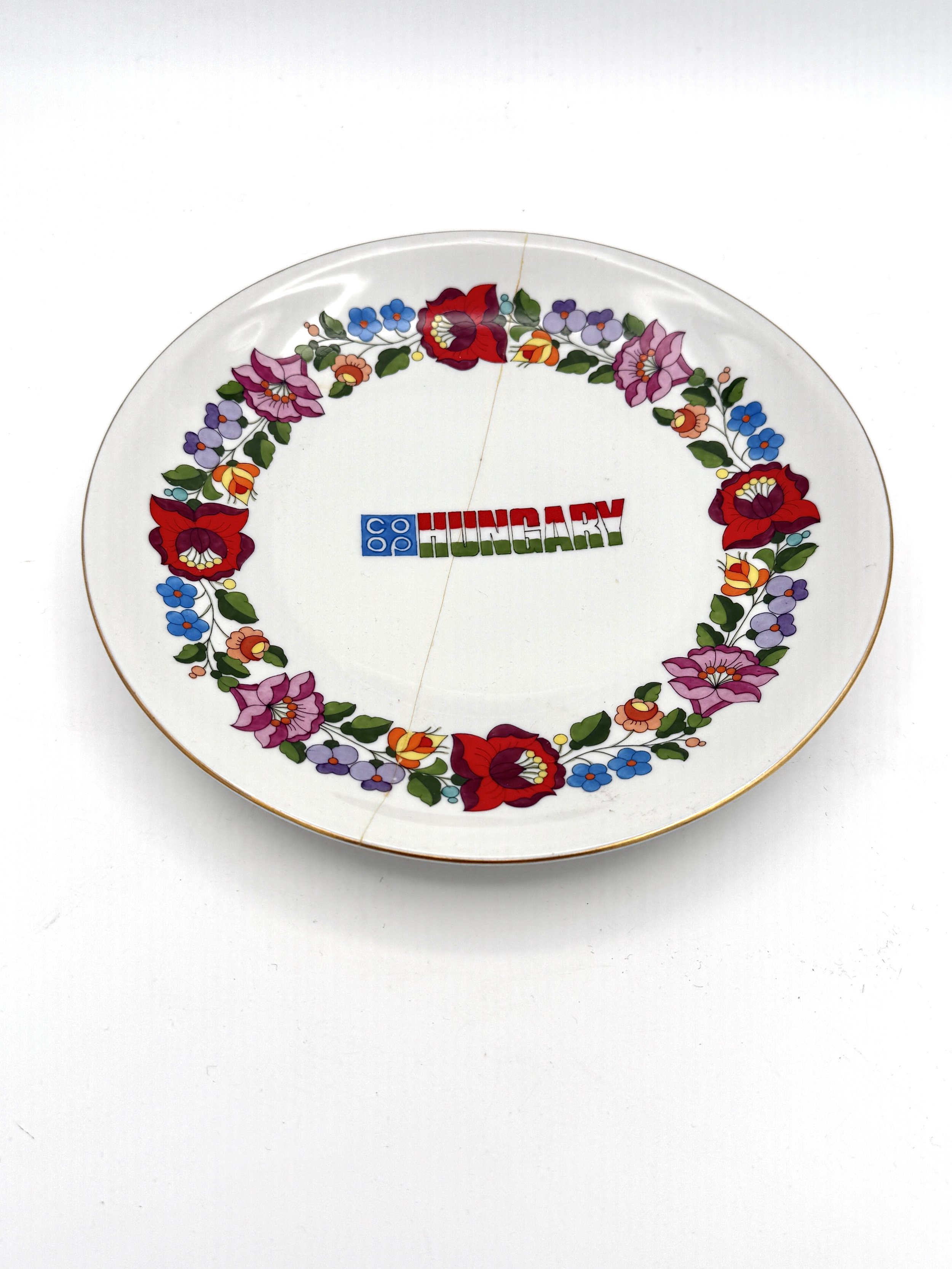 A decorative oval plate with a floral pattern around the border, displaying the word 'HUNGARY' in colorful letters at the center.