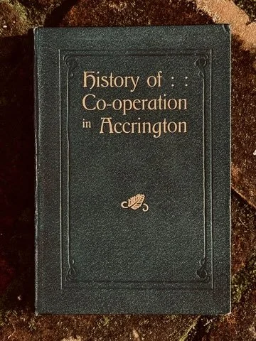 A black book titled "History of Co-operation in Accrington" with gold lettering and a small decorative emblem on the cover.