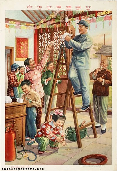 A group of children and adults in a decorated room, watching a man on a ladder handing out something, with smiles and excitement.
