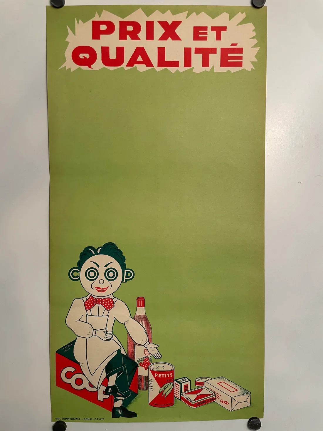 A vintage-style poster with a green background shows a cartoon character of a woman with a mime-like face, sitting on a red box labeled "COOP". She's holding a fork and surrounded by canned and boxed food items including a bottle, a tin labeled "PETI
