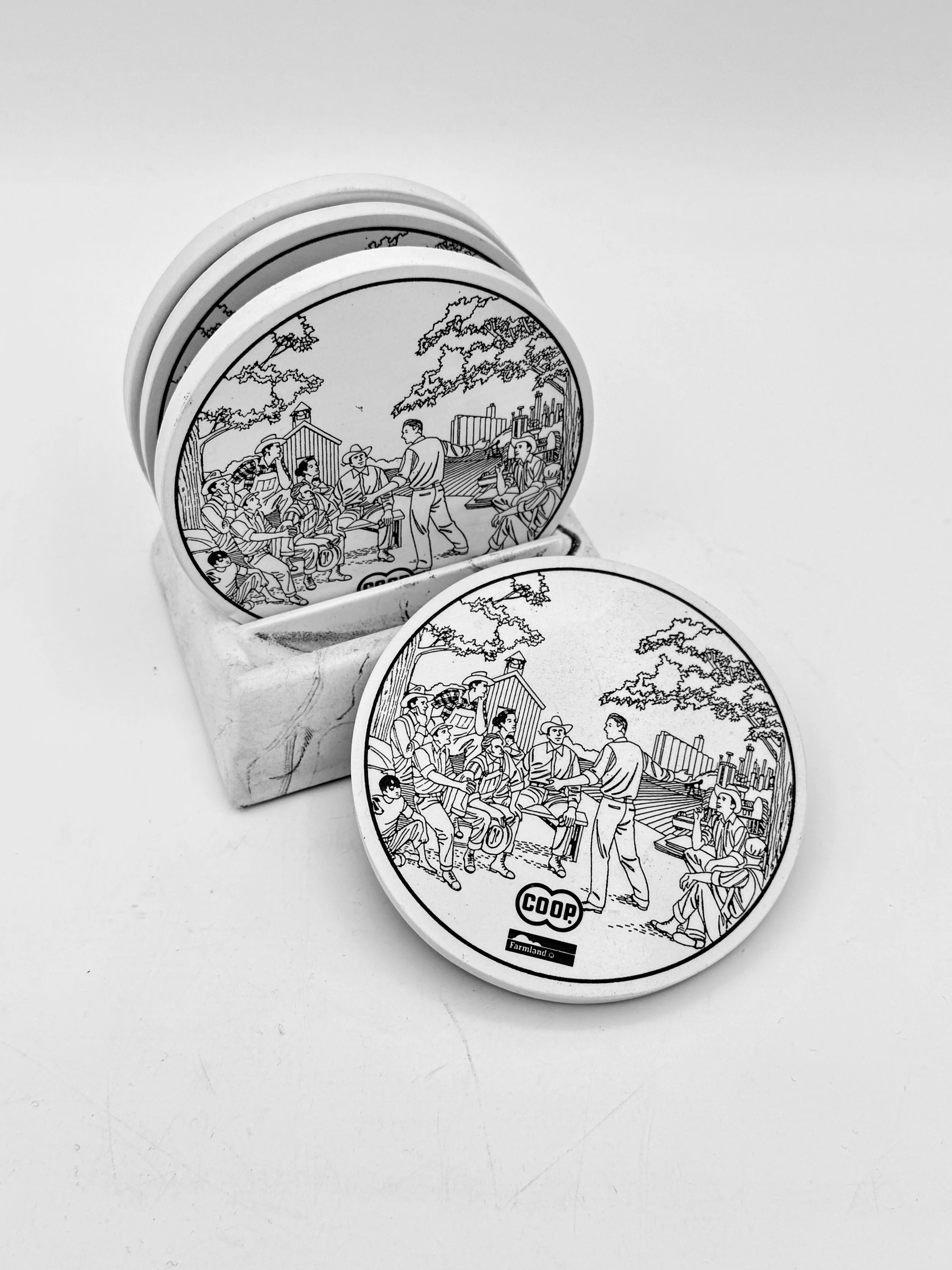 Black-and-white photo of several round tokens with cartoon illustration of people, some sitting, some standing, in a park setting with trees and a city skyline in the background. The tokens are in a small box and one is placed outside.
