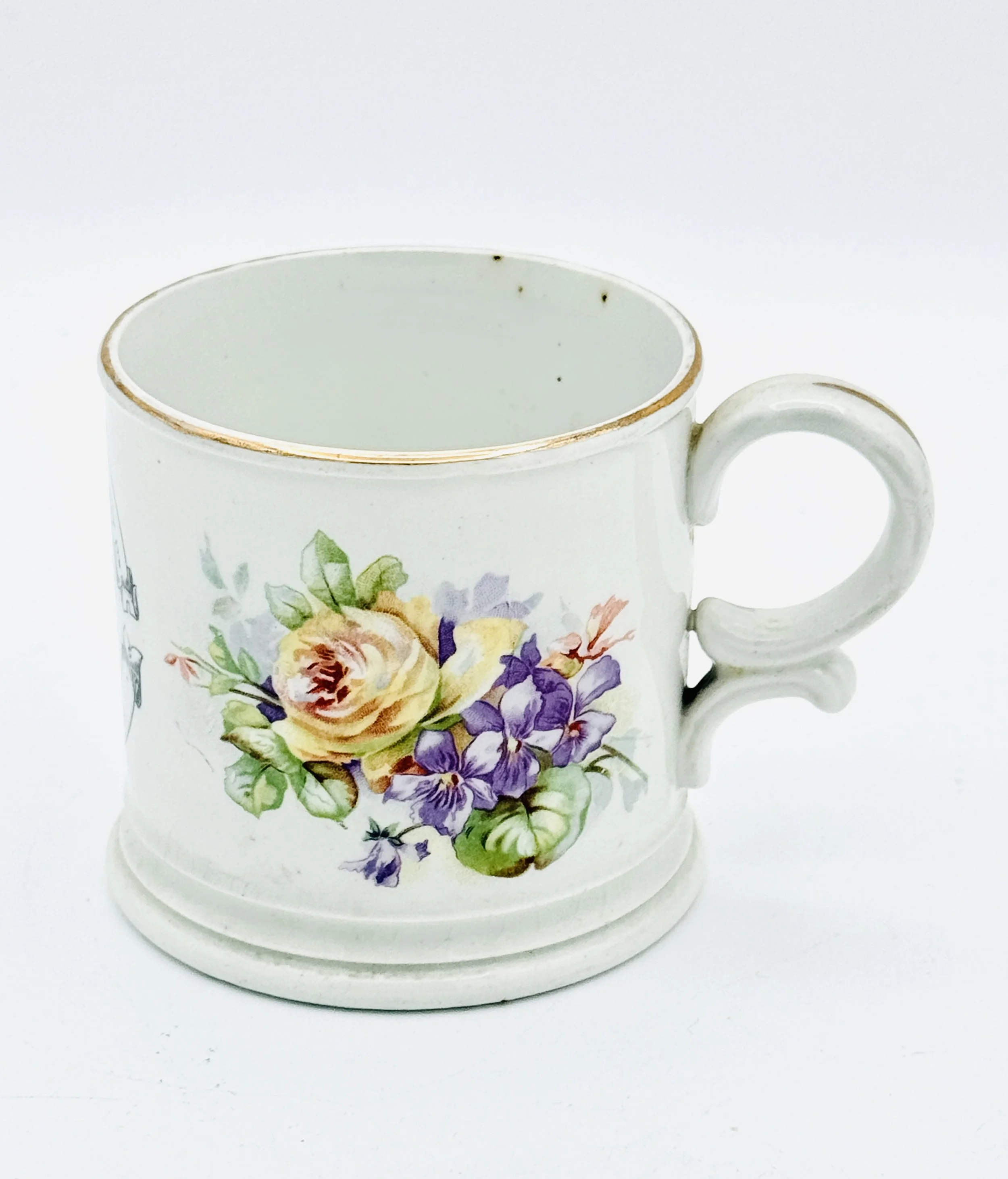 White ceramic mug with floral pattern of yellow, purple, and green flowers, resting on a matching saucer with a gold rim.