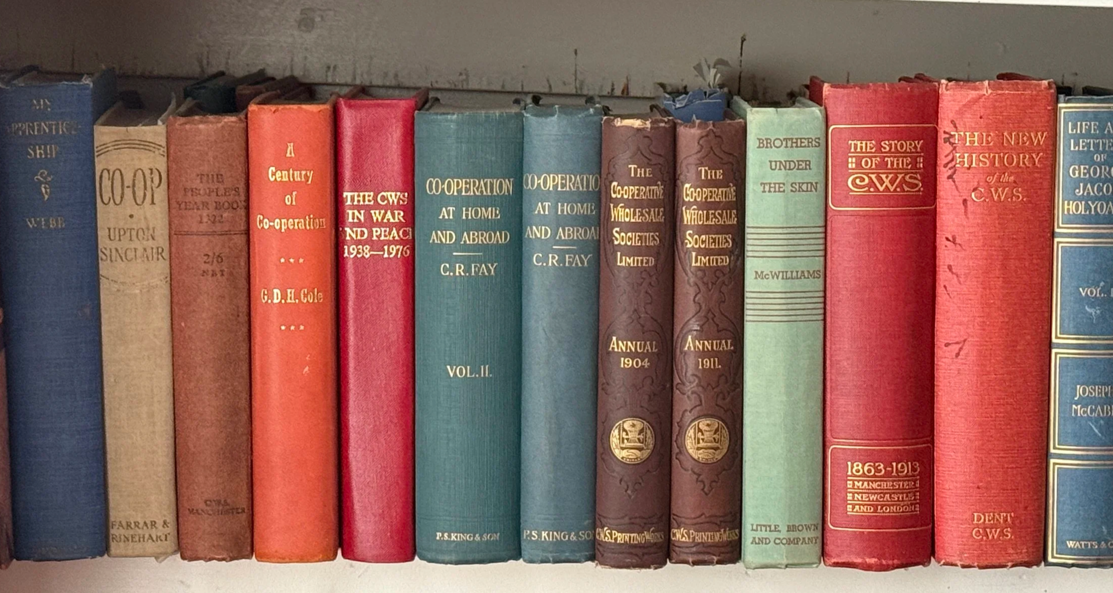 A bookshelf filled with books, including titles on cooperation, history, and George Jacob Holyoake.