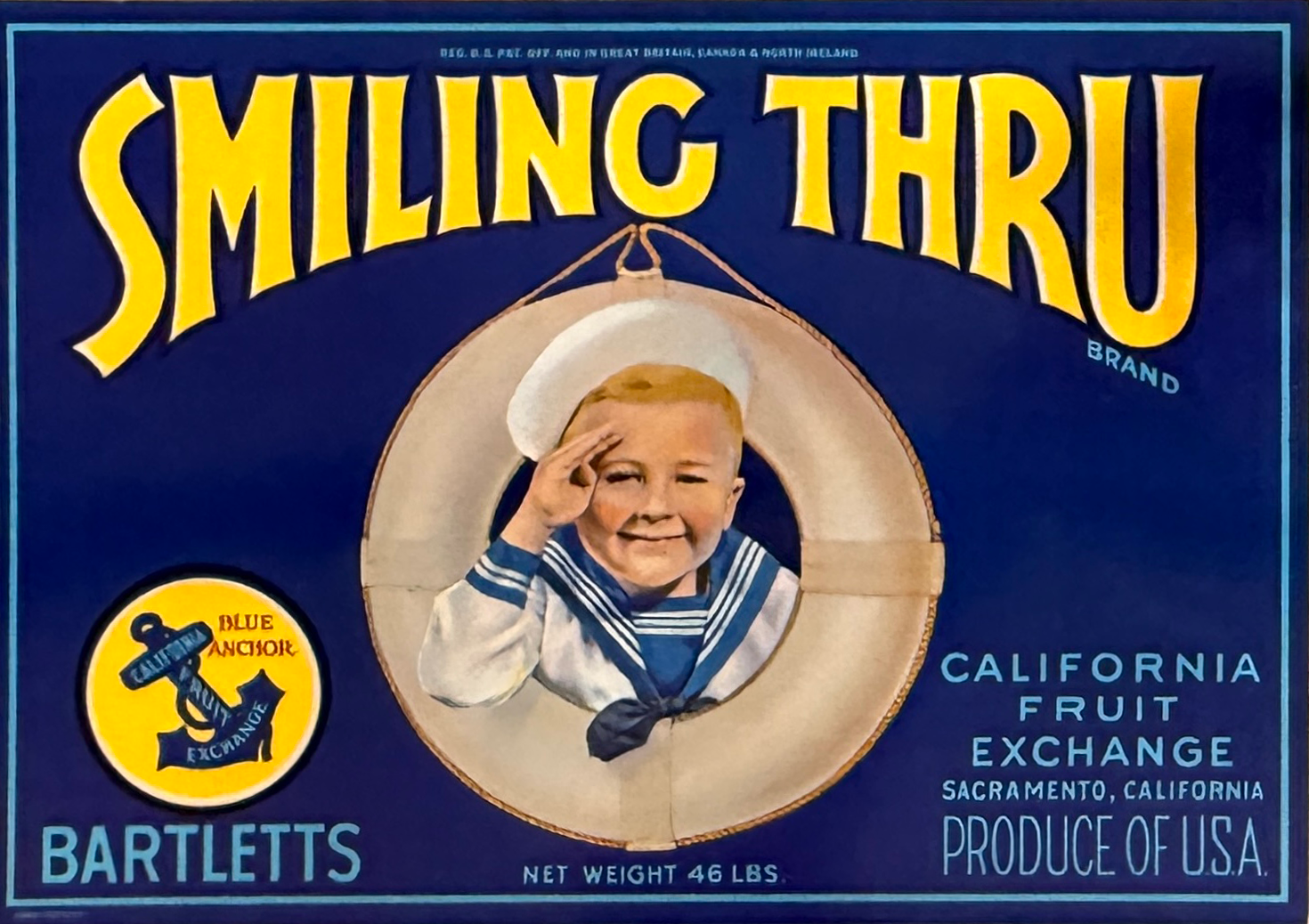 Vintage packaging for Smiling Thru brand California fruit exchange with a smiling child in a sailor outfit saluting, an anchor logo, and text indicating net weight of 46 pounds and product origin in Sacramento, USA.