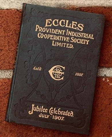 Close-up of a dark-colored anniversary booklet for Eccles Providence Industrial Cooperative Society Limited, celebrating its jubilee on July 1907, with decorative embossed lettering and design.