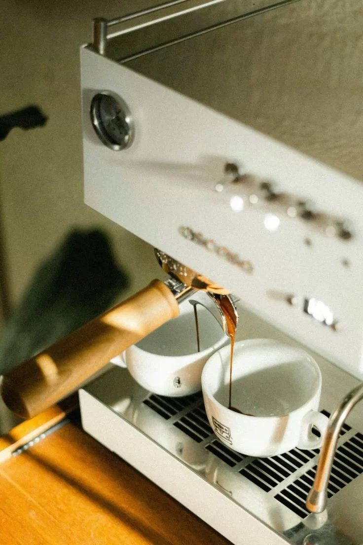 Espresso shot being pulled from a coffee machine into two white cups.