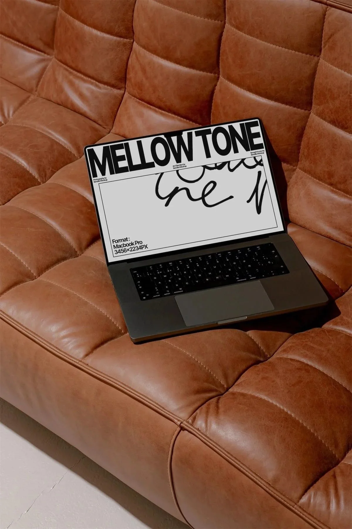 Laptop placed on a brown leather tufted couch with a display labeled 'MELLOW TONE' and handwritten black script on the screen.