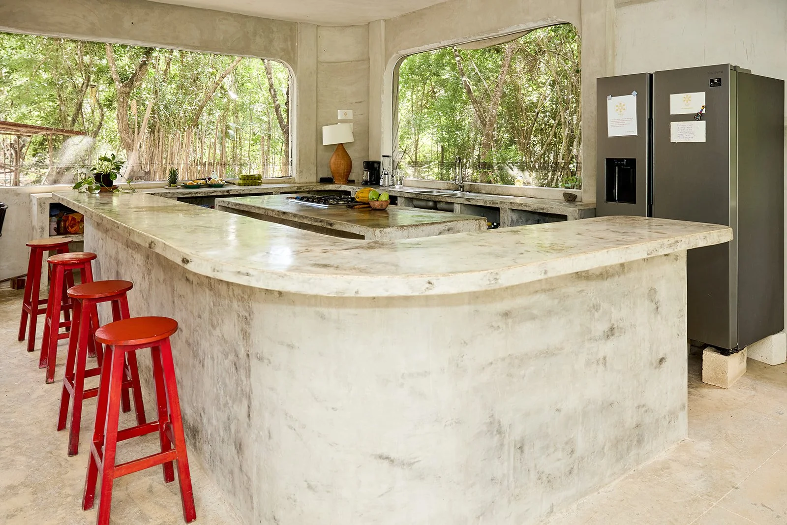 Kitchen with large curved marble countertop, red barstools, and window views of a green forest.