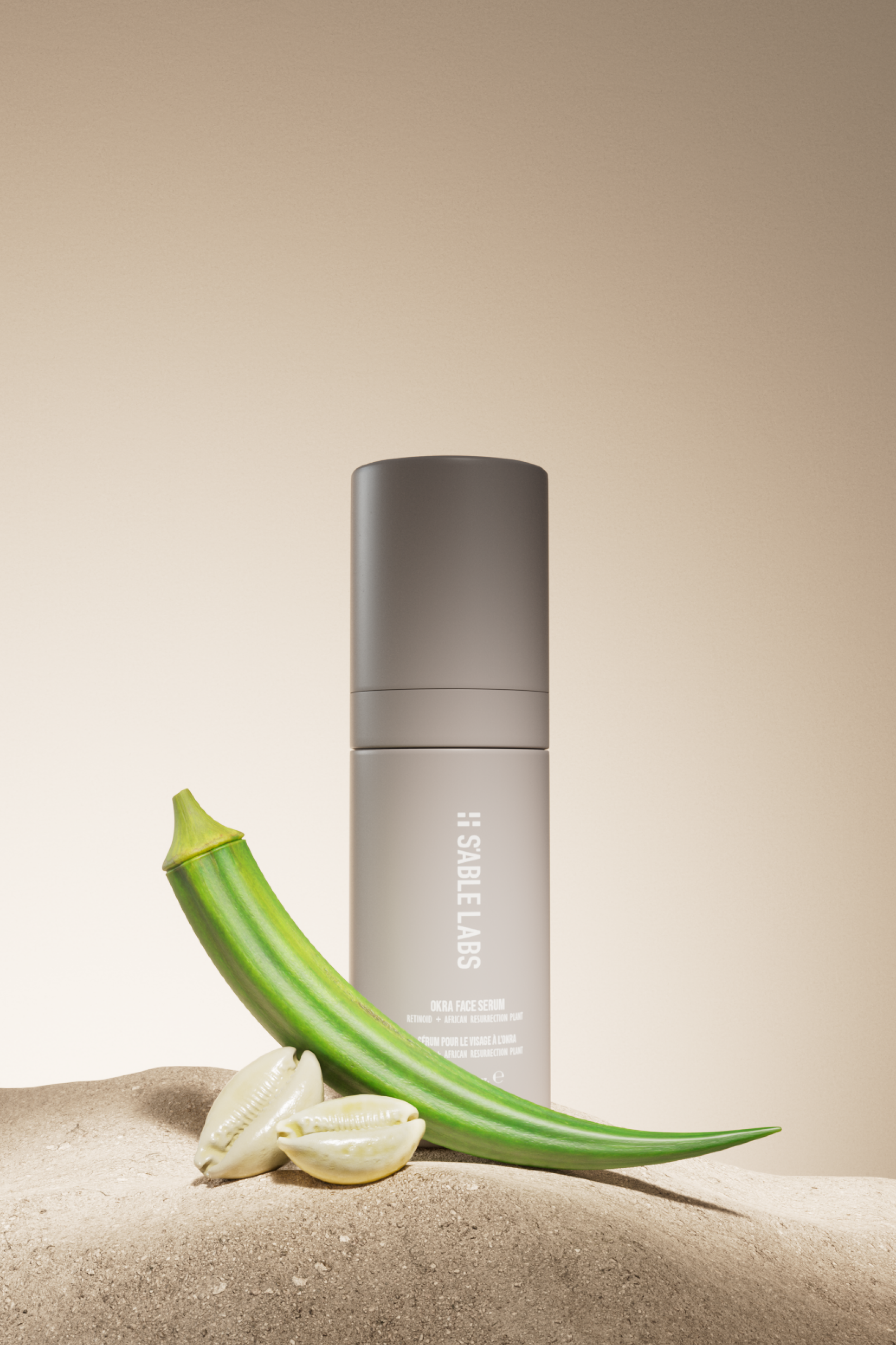 A skincare product bottle labeled 'H: SABELLÉ LABS' placed on sand next to a green cactus, a few white seashells, and a green aloe vera leaf in the foreground, with a beige gradient background.