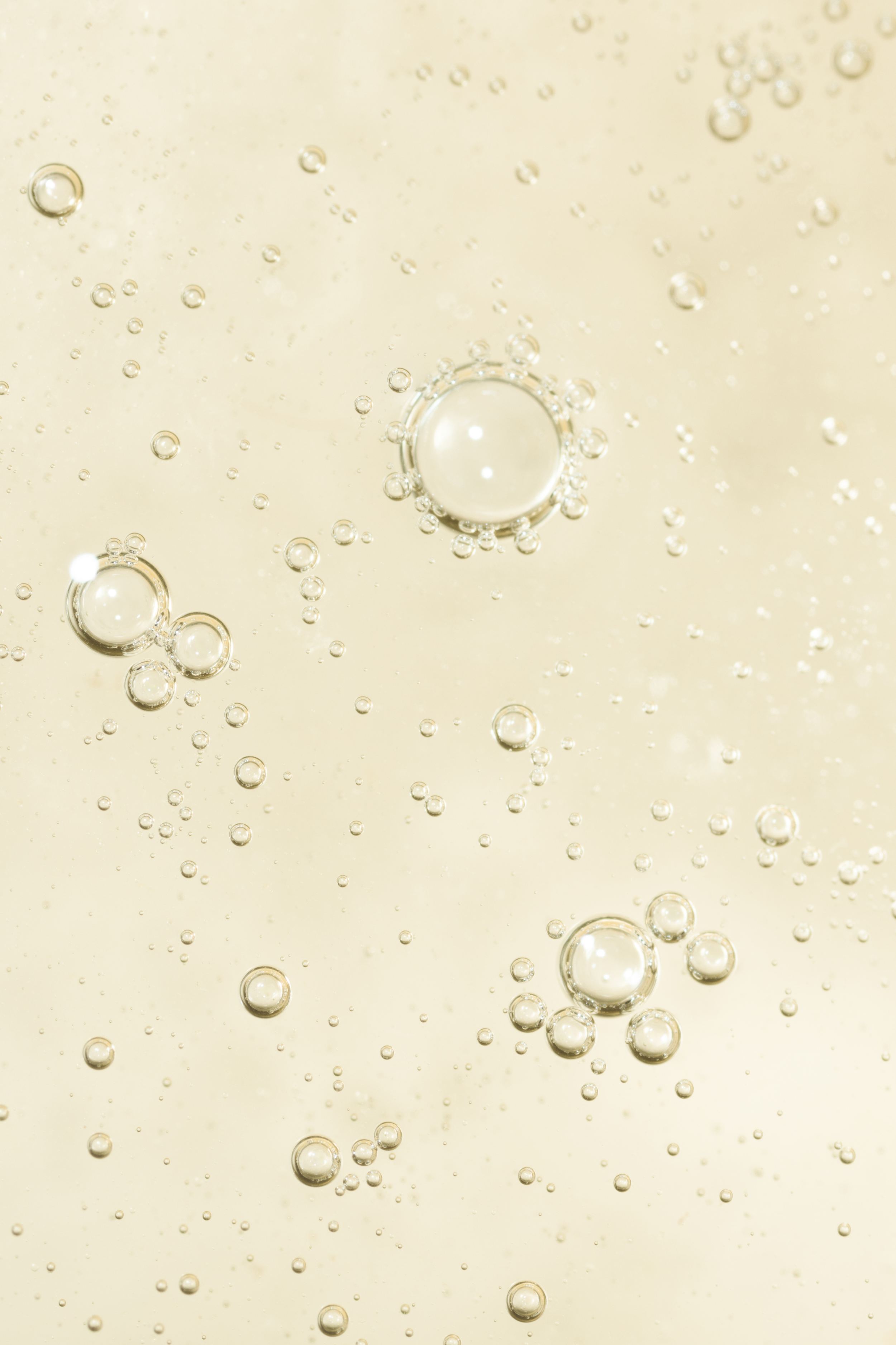 Close-up photograph of bubbles rising in a clear, pale yellow liquid, likely carbonated beverage or oil.