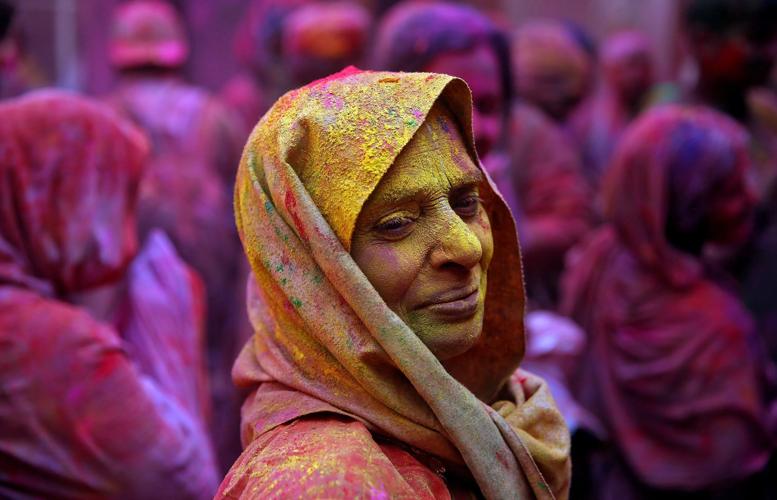 A woman covered in yellow, pink, and green powder, celebrating during the Holi festival.