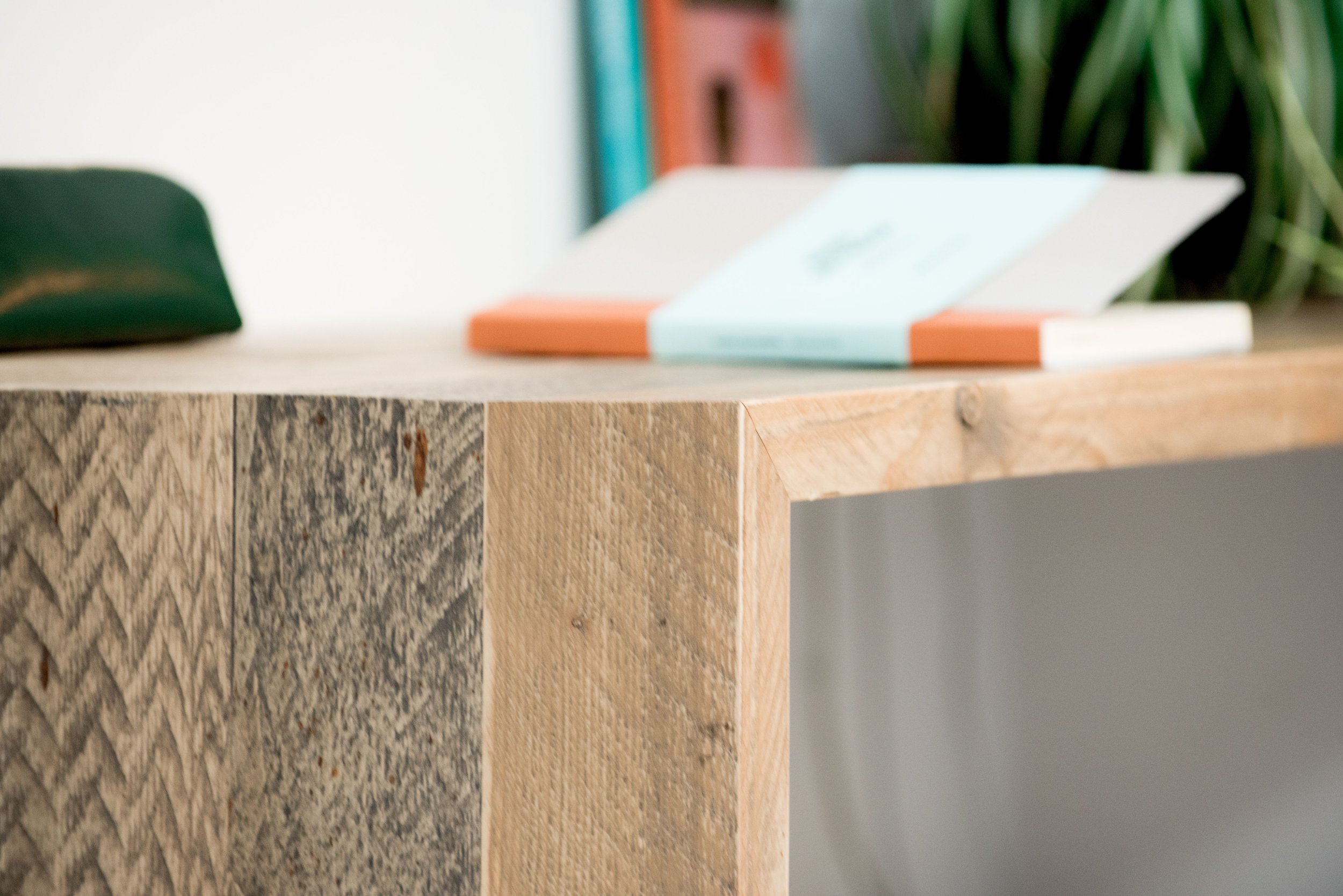 Close-up of a rustic wooden table with a stack of books and a plant in the background.