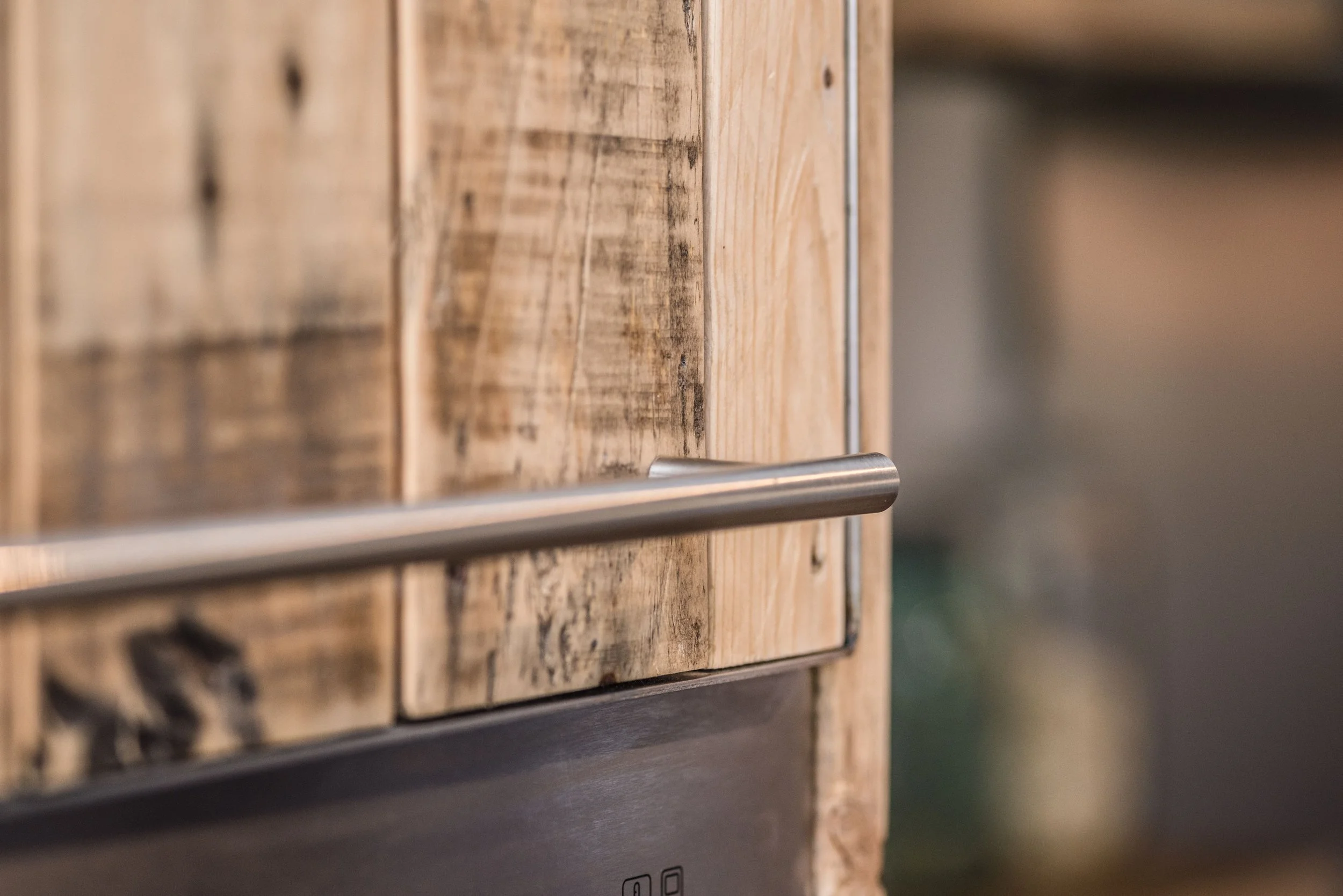 Close-up of a kitchen cabinet made of rustic wood with a stainless steel handle.