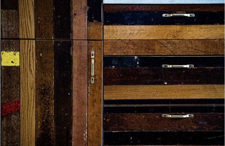 Stacked wooden pallets or crates in various shades of brown and black, with metal handles and hinges.