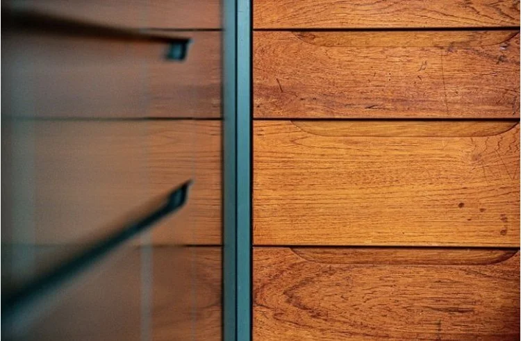 Close-up of wooden paneling with a metal divider in the center, showing contrasting textures and colors of wood.