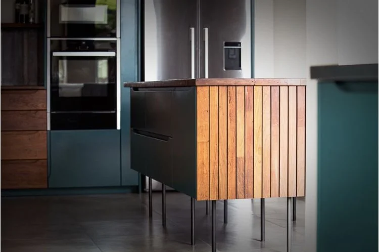 Modern kitchen with reclaimed strips of Iroko casing the sides of the kitchen islandwooden island. Kitchen shows built-in appliances.