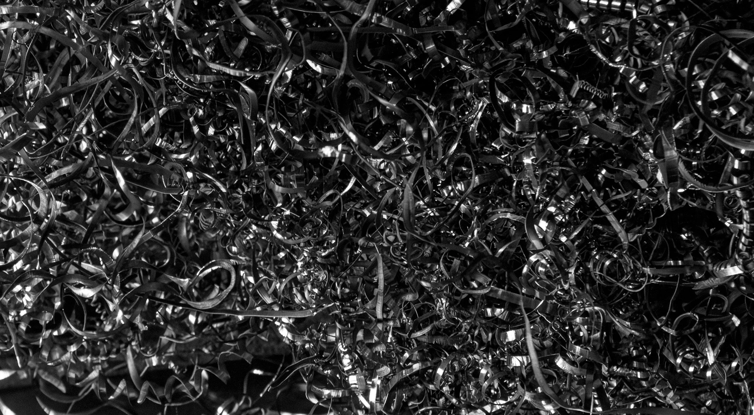 Close-up of a pile of tangled metallic chips, shiny and reflective, in black and white.