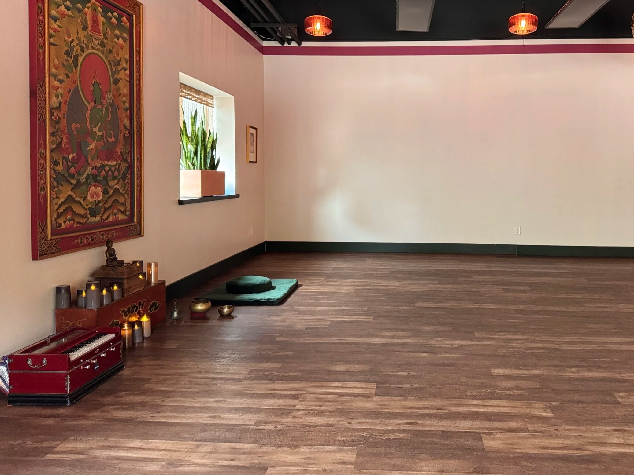 A zen meditation and yoga space at Sukha Yoga Austin. with dark wooden floors, an altar with candles, and Buddha statue. There is a framed Buddhist painting of the Green Tara deity hanging on the wall.