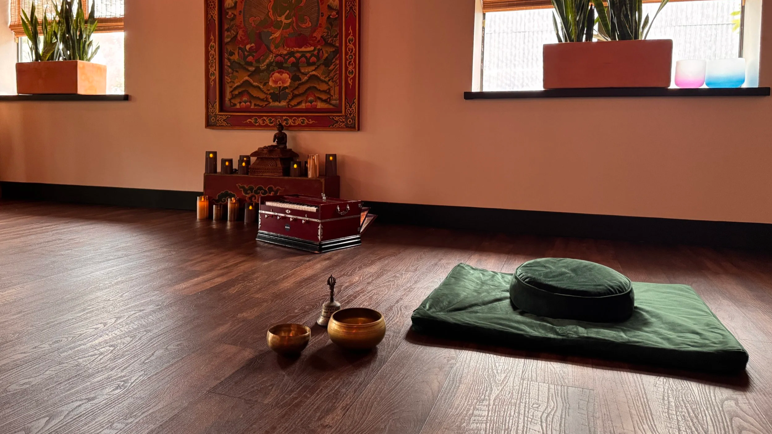 A peaceful meditation corner at Sukha Yoga Austin. A velvet green meditation cushion invites you to slow down and imagine yourself in deep relaxation. There is an altar with a Buddha statue, candles, and an ornate Green Tara painting and windows.