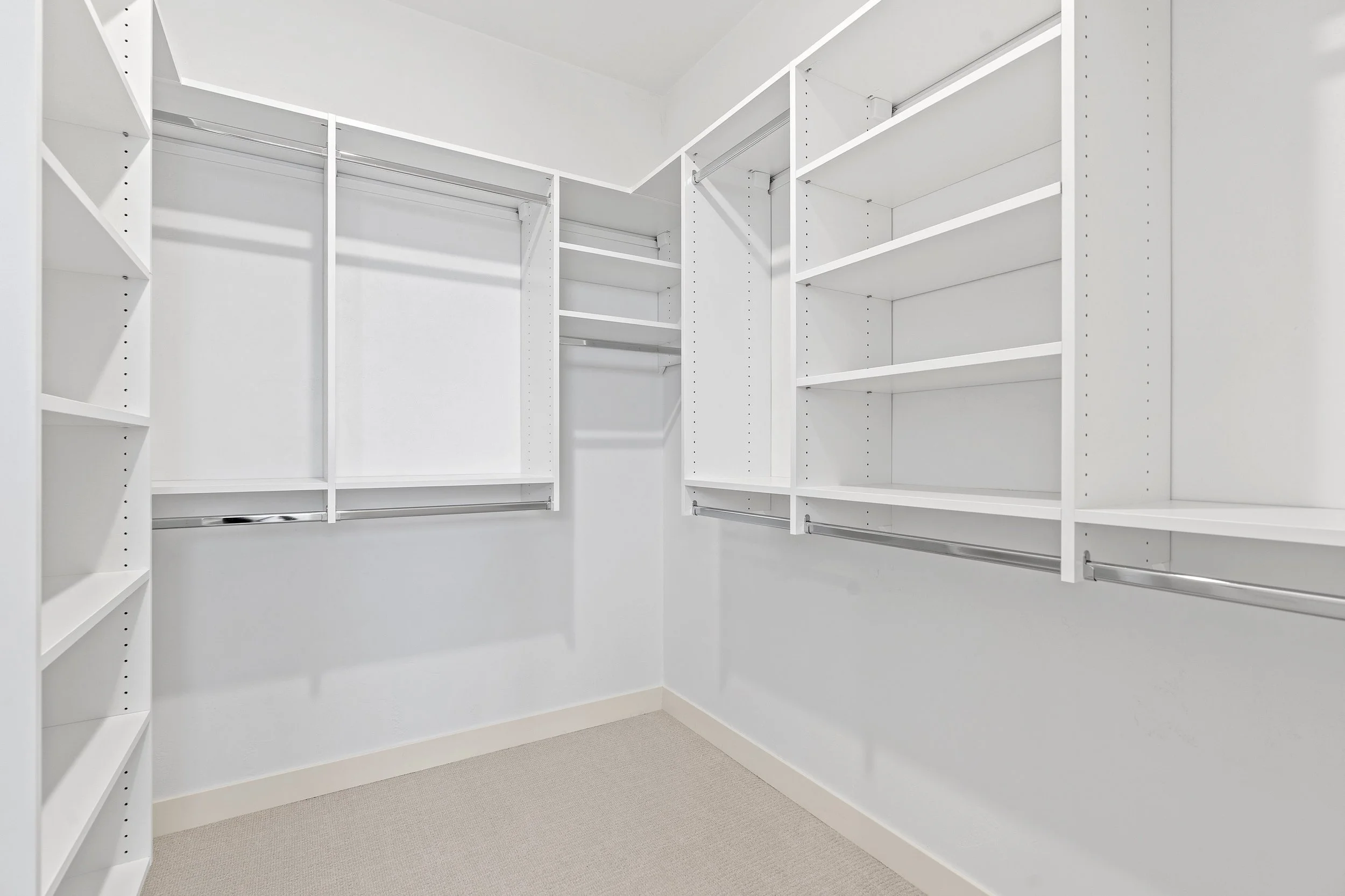 Empty white walk-in closet with built-in shelves and hanging rods.